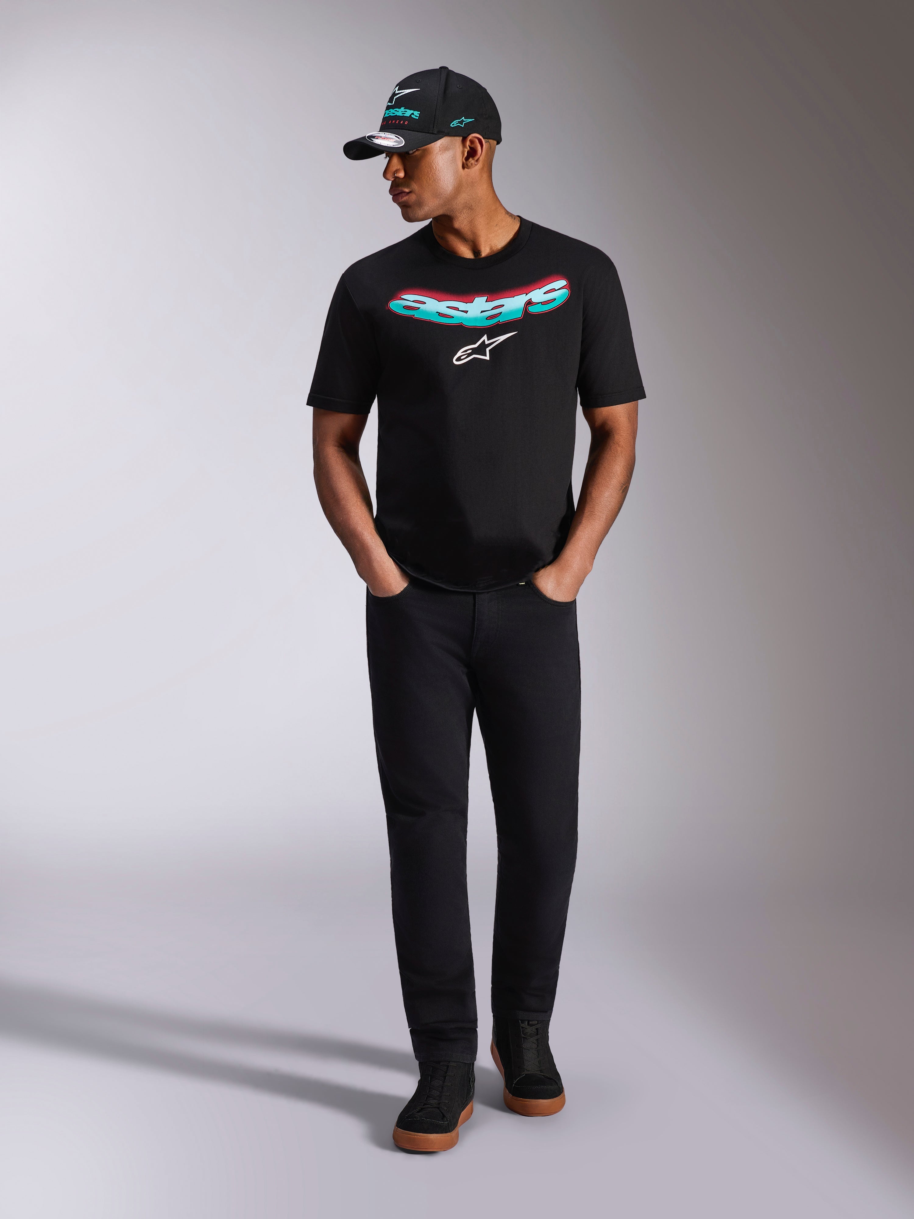 Alpinestars Ellipsoid CSF Tee, Short Sleeve T-Shirt, Black, Teal and Pink Gradient Curved Astars Wordmark with White Logo, worn by model with matching black cap and pants, casual motorsport lifestyle wear
