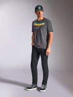 Alpinestars Ellipsoid CSF Tee, T-shirt met korte mouwen, antracietgrijs, met gebogen Astars-woordmerk met kleurverloop en wit logo, gedragen door model met zwarte broek en pet, casual motorsport streetwear