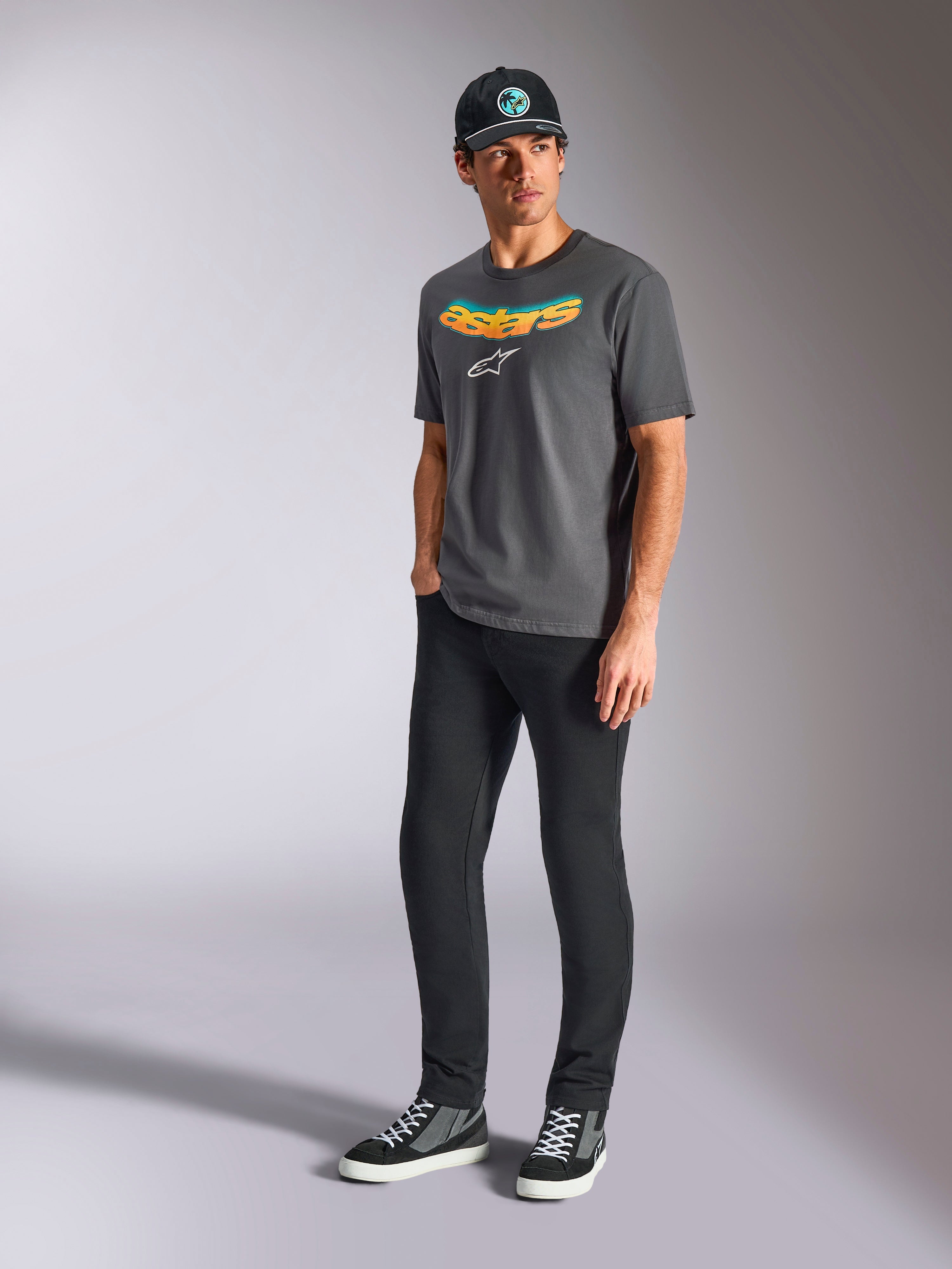 Alpinestars Ellipsoid CSF Tee, T-shirt met korte mouwen, antracietgrijs, met gebogen Astars-woordmerk met kleurverloop en wit logo, gedragen door model met zwarte broek en pet, casual motorsport streetwear