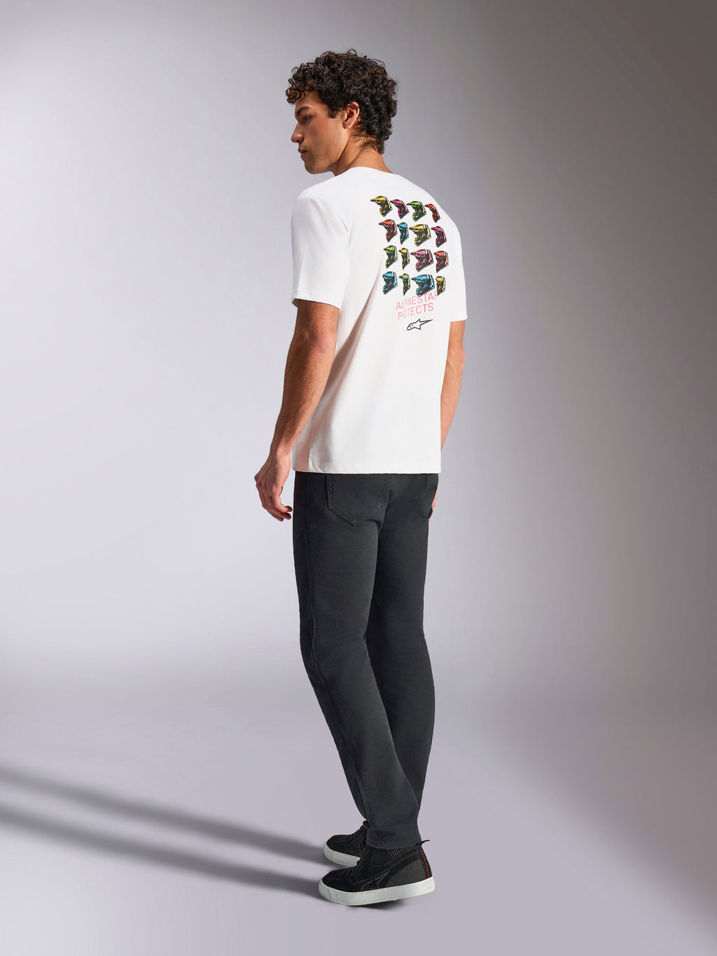 Alpinestars Pop Helmet CSF Tee, wit T-shirt met korte mouwen, achteraanzicht op model met kleurrijke M10 helm graphics, gestyled met een donkere broek en zwarte sneakers, casual motorsport-geïnspireerde streetwear