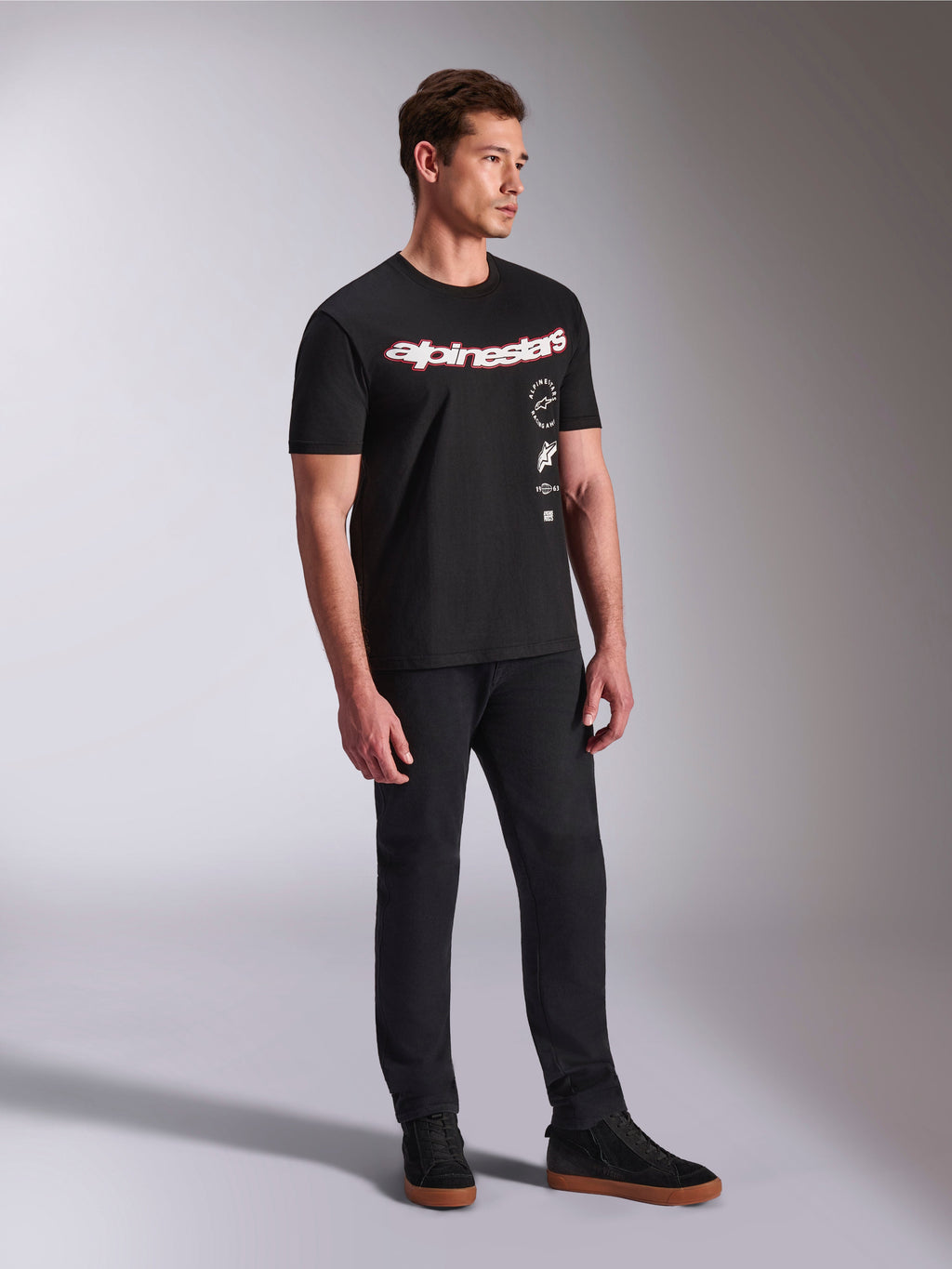Alpinestars Abus CSF Tee, Short Sleeve T-Shirt, Black, featuring curved red and white Alpinestars logo with vertical stacked graphics, worn with black pants and sneakers, casual motorsport-inspired streetwear