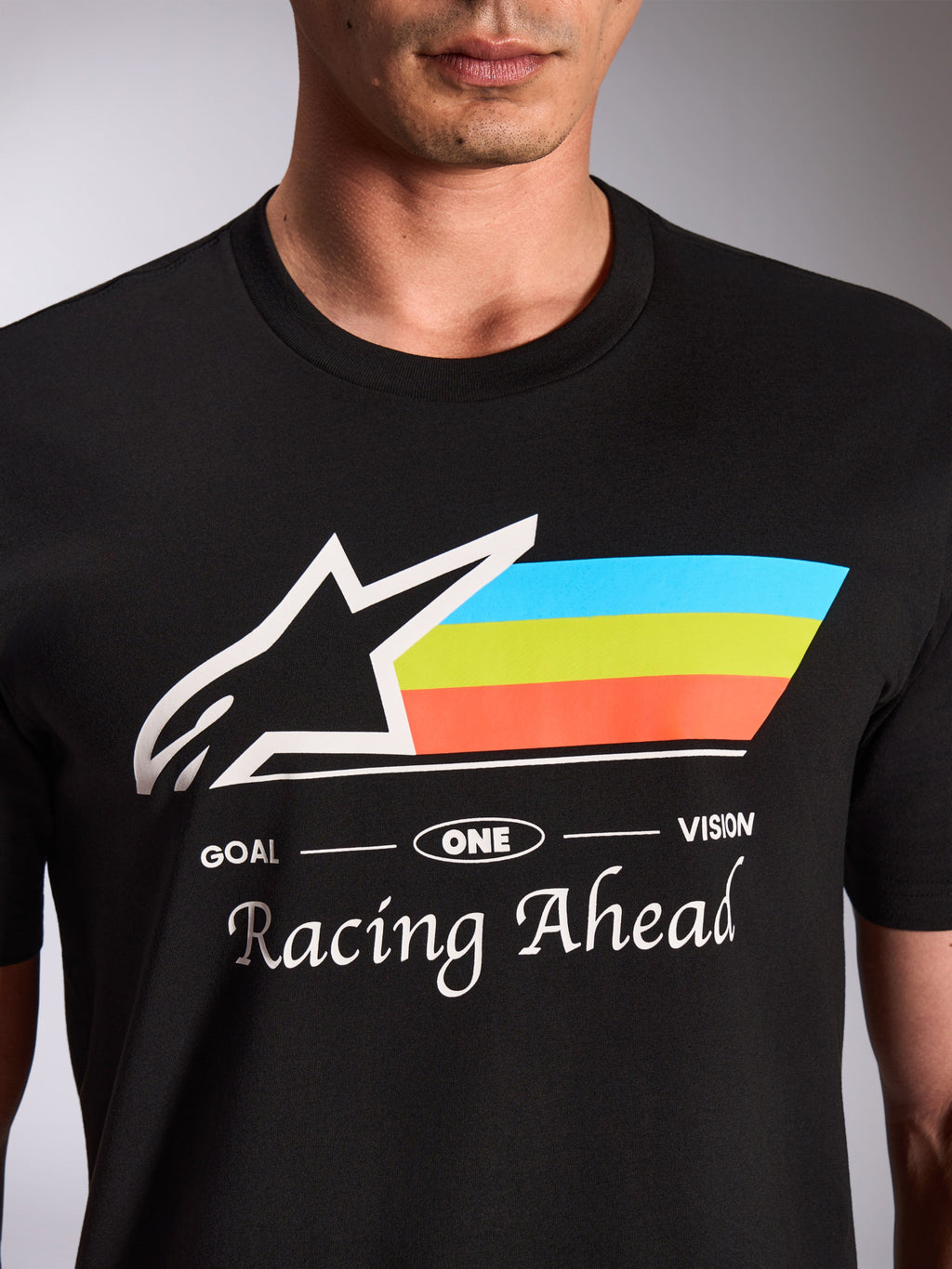Alpinestars Trifecta CSF Tee, T-shirt met korte mouwen, zwart, close-up van de grafische print op de voorzijde met wit Astars-logo en driekleurige blauwe, groene en oranje strepen, tekst 'Racing Ahead', casual motorsport streetwear