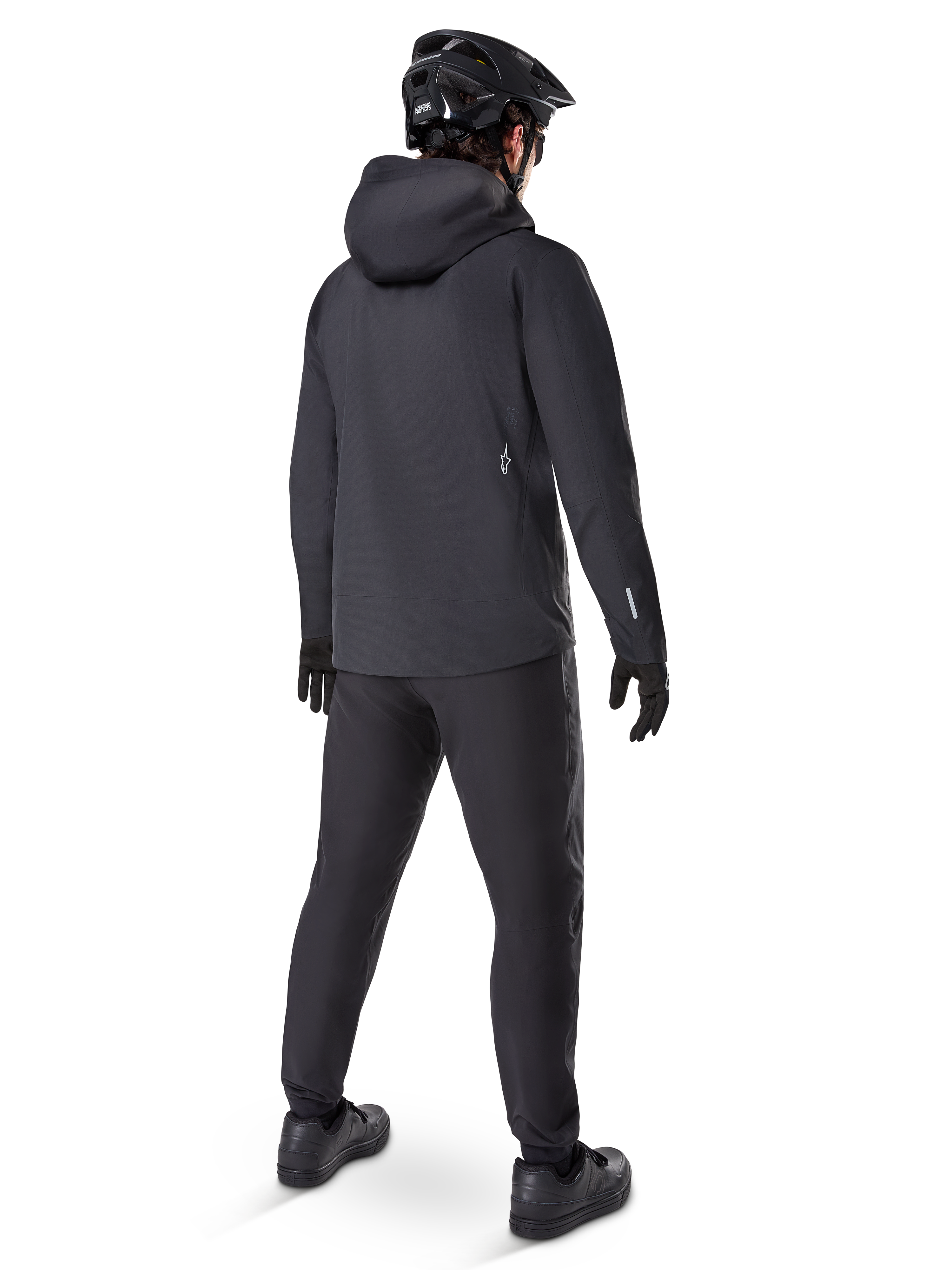 Alpinestars A-Dura Elite Waterdichte Jas, Zwart, achteraanzicht met capuchon over de helm en een verlengde achterzoom, gecombineerd met bijpassende zwarte MTB-broek, handschoenen en helm voor volledige trailbescherming in alle weersomstandigheden.