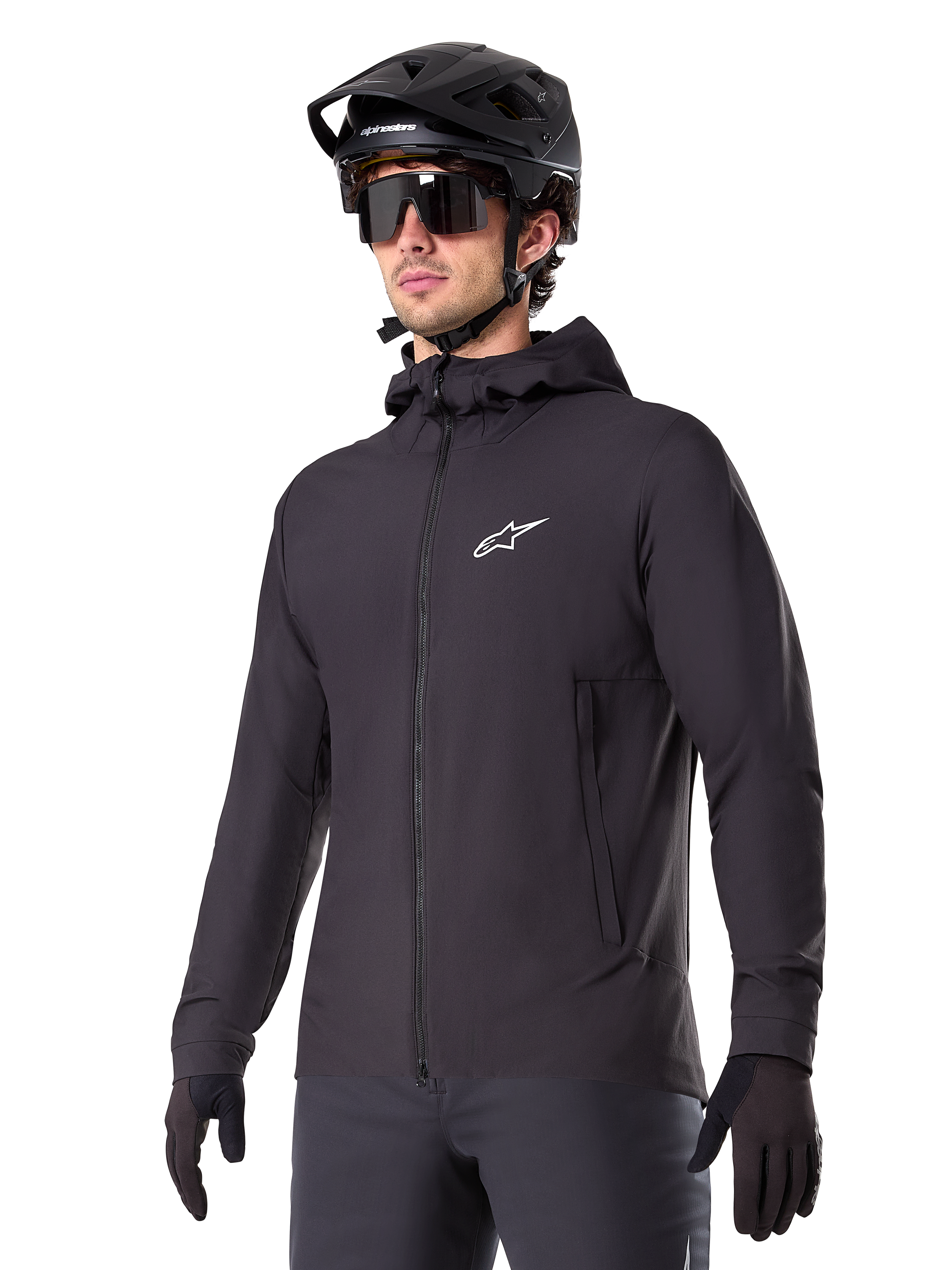 Alpinestars A-Dura Thermal Jacket, zwarte fietsjas, ontwerp met capuchon en ritssluiting aan de voorzijde, wit sterlogo op de borst, gedragen met zwarte mountainbikehelm en handschoenen, sportieve prestatiekleding voor trailrijden in koud weer