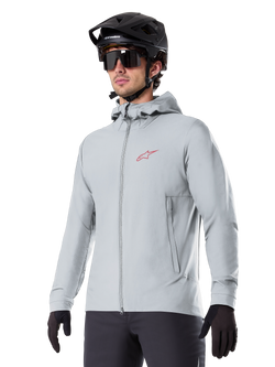 Alpinestars A-Dura Thermal Jacket, light gray insulated cycling jacket, hooded design with a small red logo, worn with a black helmet and gloves, technical mountain bike apparel for cold-weather riding