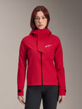 Alpinestars Stella A-Dura Elite waterdichte jas, mountainbikejas voor dames, fluorood, ontwerp met capuchon en asymmetrische voorflap, wit Alpinestars-logo op de borst, verstelbare zwarte manchetten, gedragen door een vrouwelijk model met zwarte broek