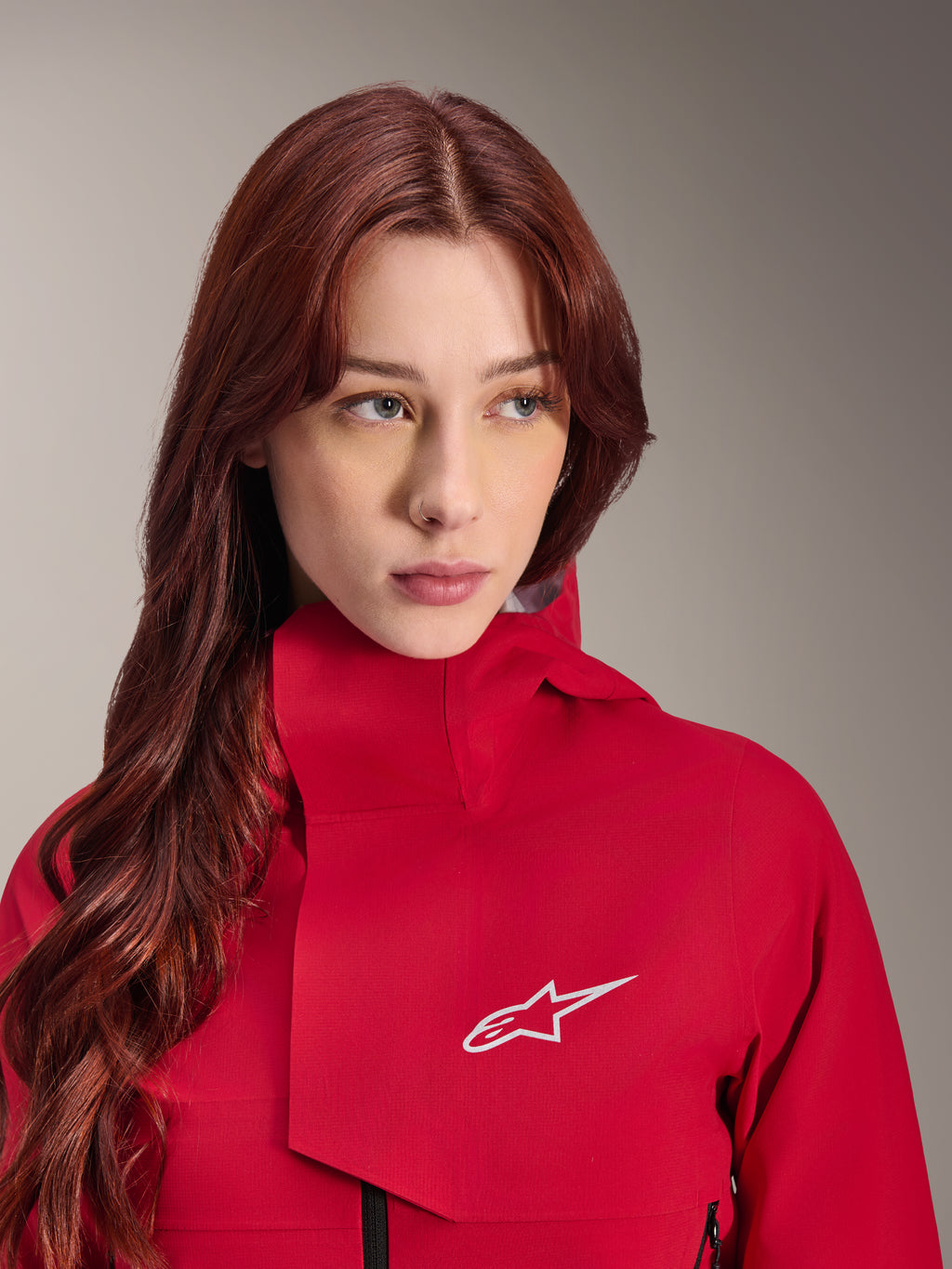 Alpinestars Stella A-Dura Elite Waterdichte Jas, Red Fluo, gedragen door een vrouw met lang rood haar, technische 3-laags waterdichte jas met hoge kraag en wit logo, hoogwaardige outdoor- en mountainbike-uitrusting
