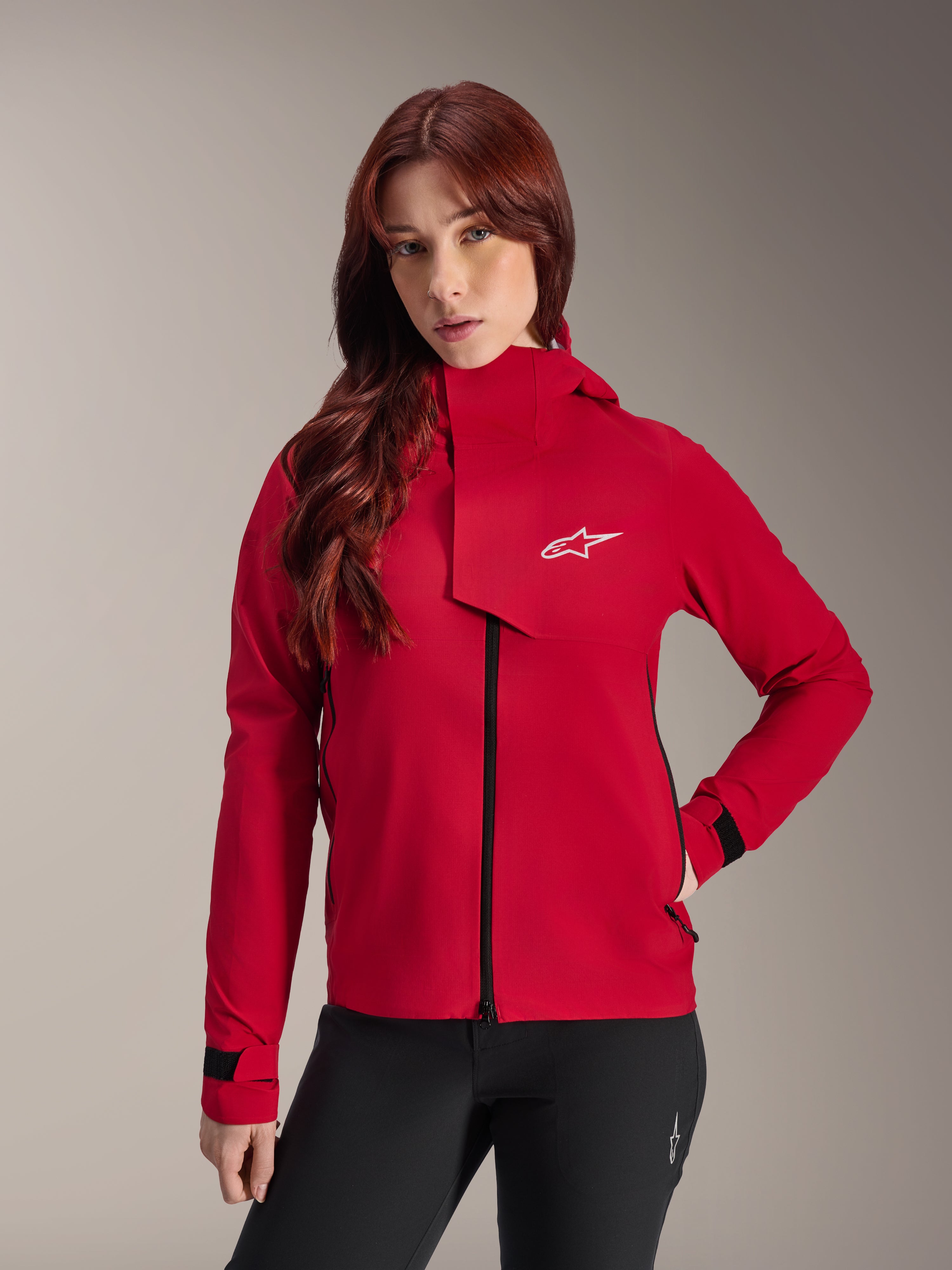 Alpinestars Stella A-Dura Elite Waterdichte Jas, mountainbikejas voor dames, Red Fluo, met een stormflap aan de voorzijde voorzien van een wit Alpinestars-logo, hoge kraag en verstelbare manchetten, gedragen met een zwarte broek voor een technische rijlook