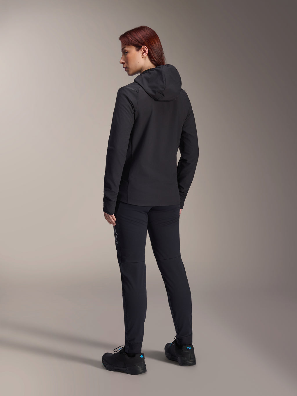 Alpinestars Stella A-Dura Thermal Jacket, MTB-fietsjack voor dames, zwart, achteraanzicht met focus op de geïsoleerde capuchon en normale pasvorm, gedragen met bijpassende zwarte broek en schoenen, lichtgewicht thermische isolatie voor ritten in koud weer