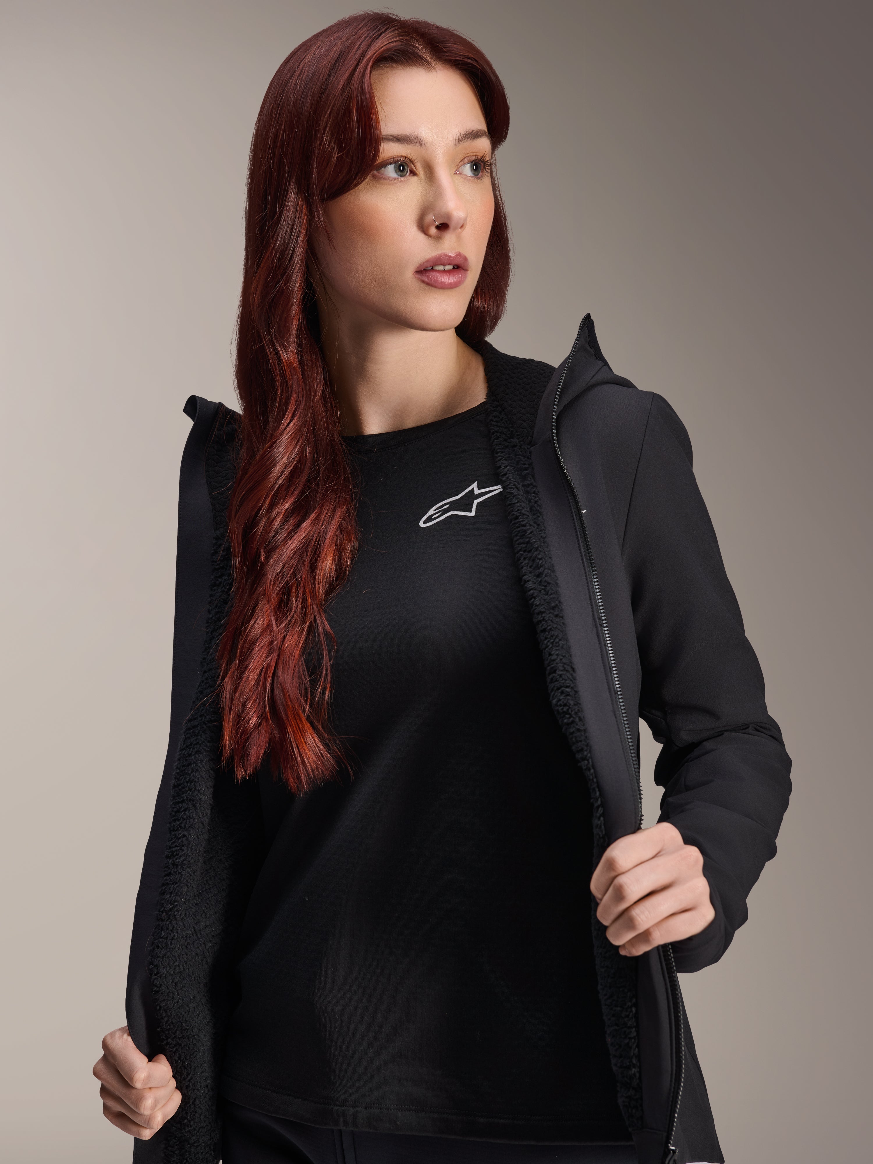 Alpinestars Stella A-Dura Thermojas, zwart dames fietsjack, open getoond met getextureerde fleecevoering en ritssluiting, gedragen over een zwart T-shirt met Alpinestars-logo, lichtgewicht en geïsoleerd voor ritten in koud weer