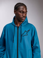 Male model wearing the Alpinestars Speeder Chromium Windbreak Jacket, Blue, lightweight hooded windbreaker, black Astars logo on chest, black front zipper and drawcords, casual motorsport-inspired streetwear