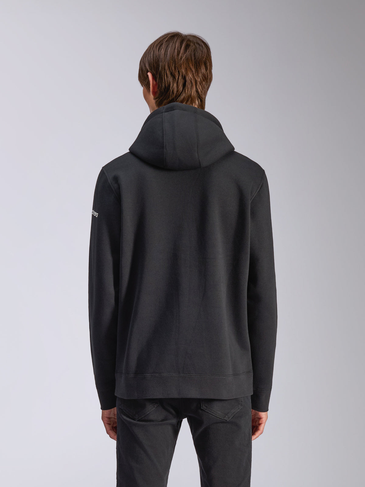 Alpinestars Frontal Hoodie, zwart, achteraanzicht van een casual pullover sweatshirt, met een zelfgevoerde capuchon, geribde zoom en wit woordmerklogo op de mouw, op motorsport geïnspireerde streetwear.