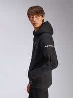 Alpinestars Frontal Hoodie, zwarte pullover fleece, model draagt item in zijaanzicht, wit Alpinestars woordmerk op de mouw, kangoeroezak, casual motorsport-geïnspireerde streetwear