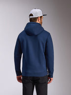 Alpinestars Frontal Hoodie, navy blue pullover fleece, back view of casual streetwear, worn with black pants and a white and black mesh cap, modern motorsport-inspired design