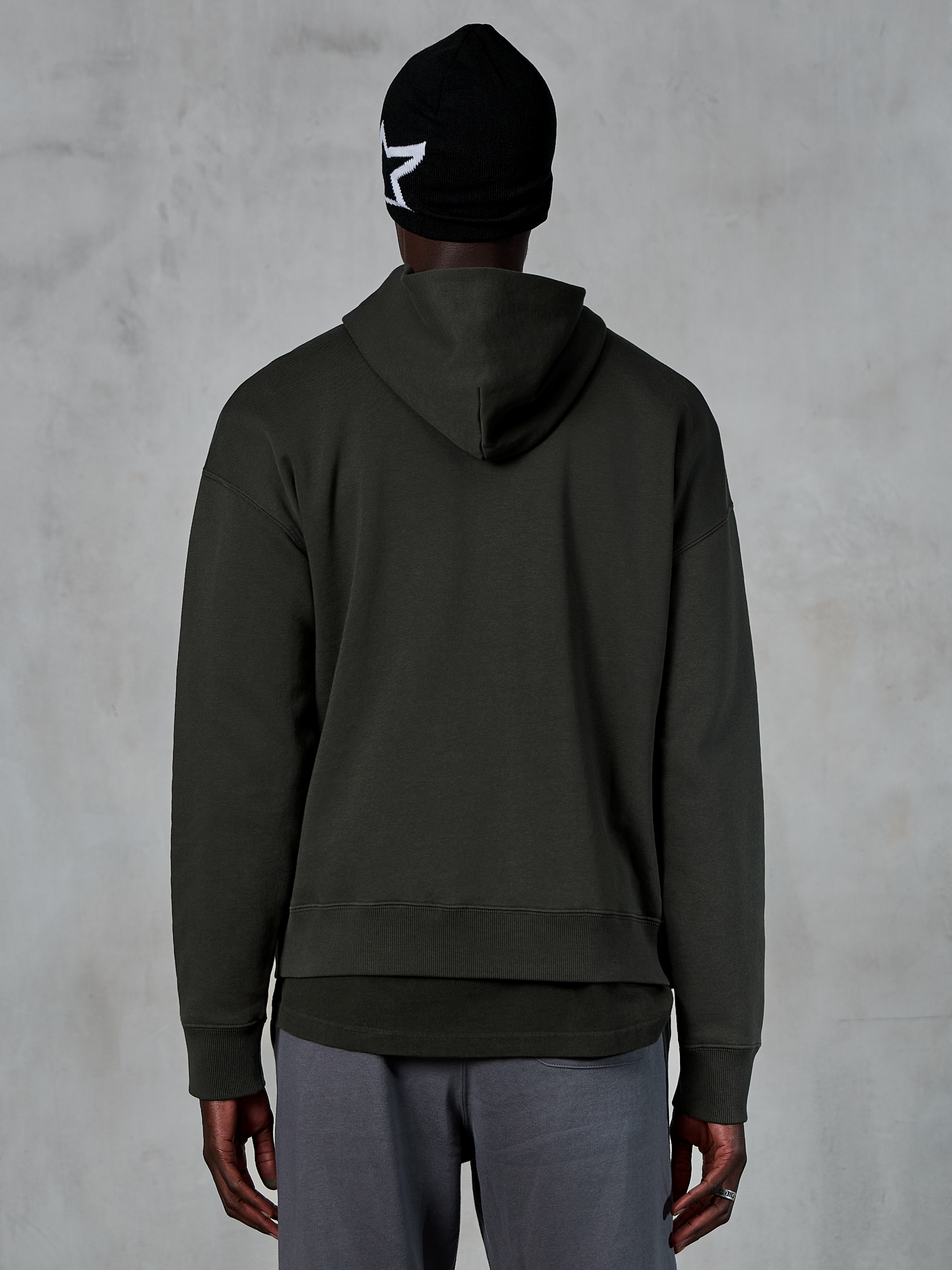 Alpinestars Essentials Ageless Hoodie, achteraanzicht, Off Black, casual streetwear, model draagt een zwarte muts met wit sterlogo en een grijze broek, premium fleece met stone-wash afwerking