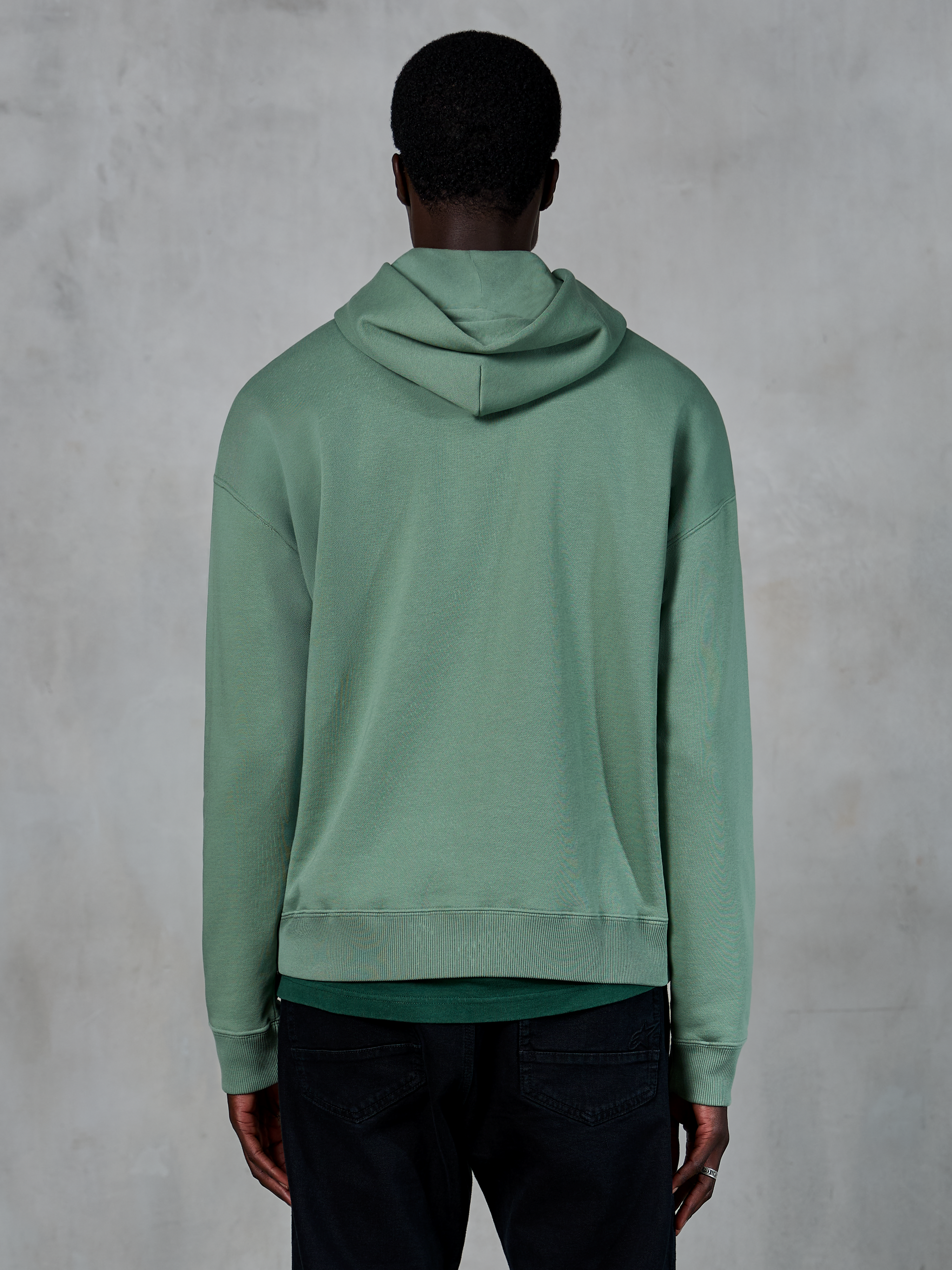 Alpinestars Essentials Ageless Hoodie, casual sportkleding, Cactusgroen, achteraanzicht op model, garment stone wash afwerking, gecombineerd met zwarte broek, minimalistisch lifestyle-ontwerp