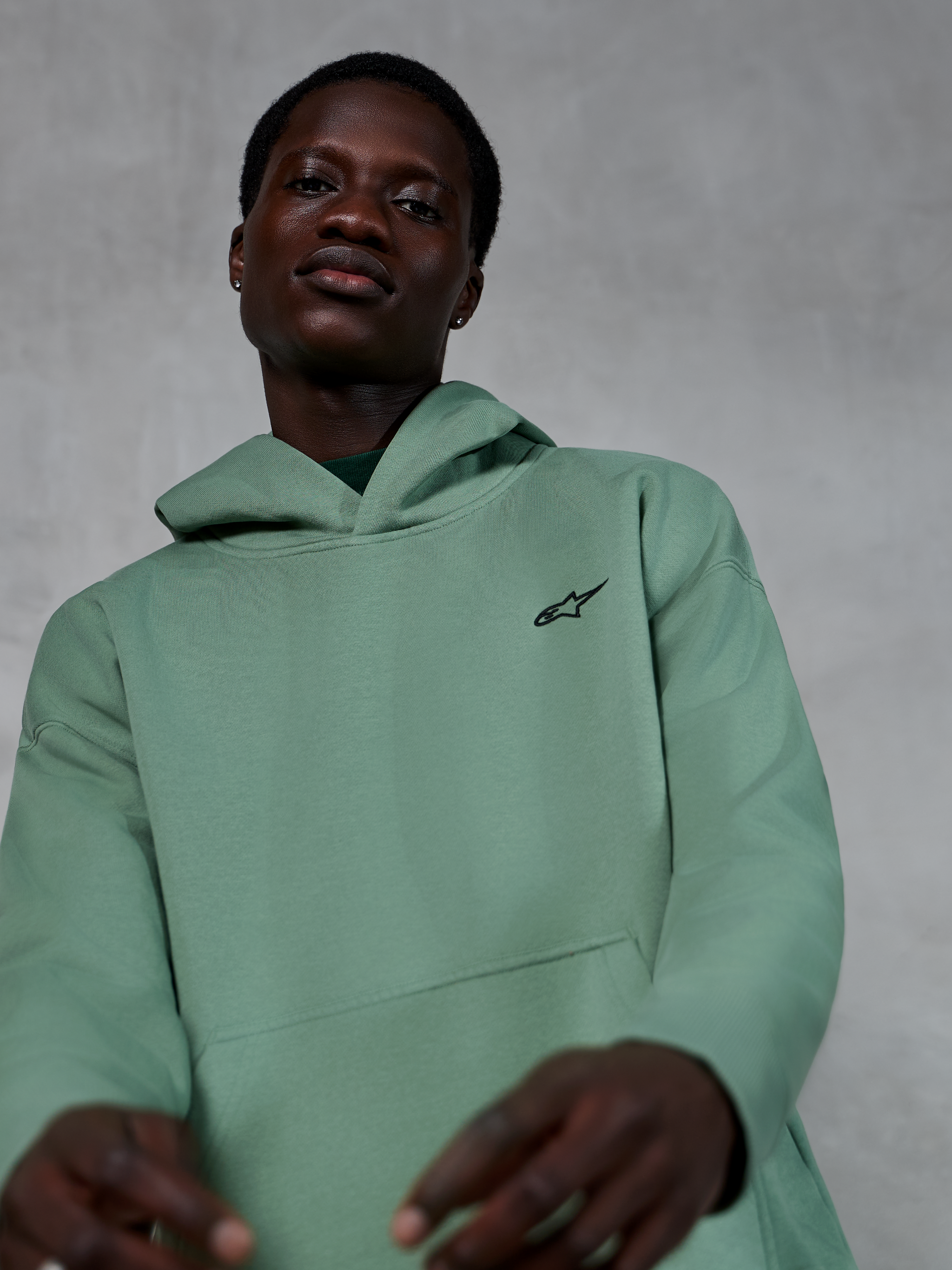 Alpinestars Essentials Ageless Hoodie, casual sportkleding in cactusgroen, gedragen door een model, met een klein zwart Alpinestars-logo op de borst, hoogwaardige fleece met een relaxte pasvorm en strakke esthetiek.