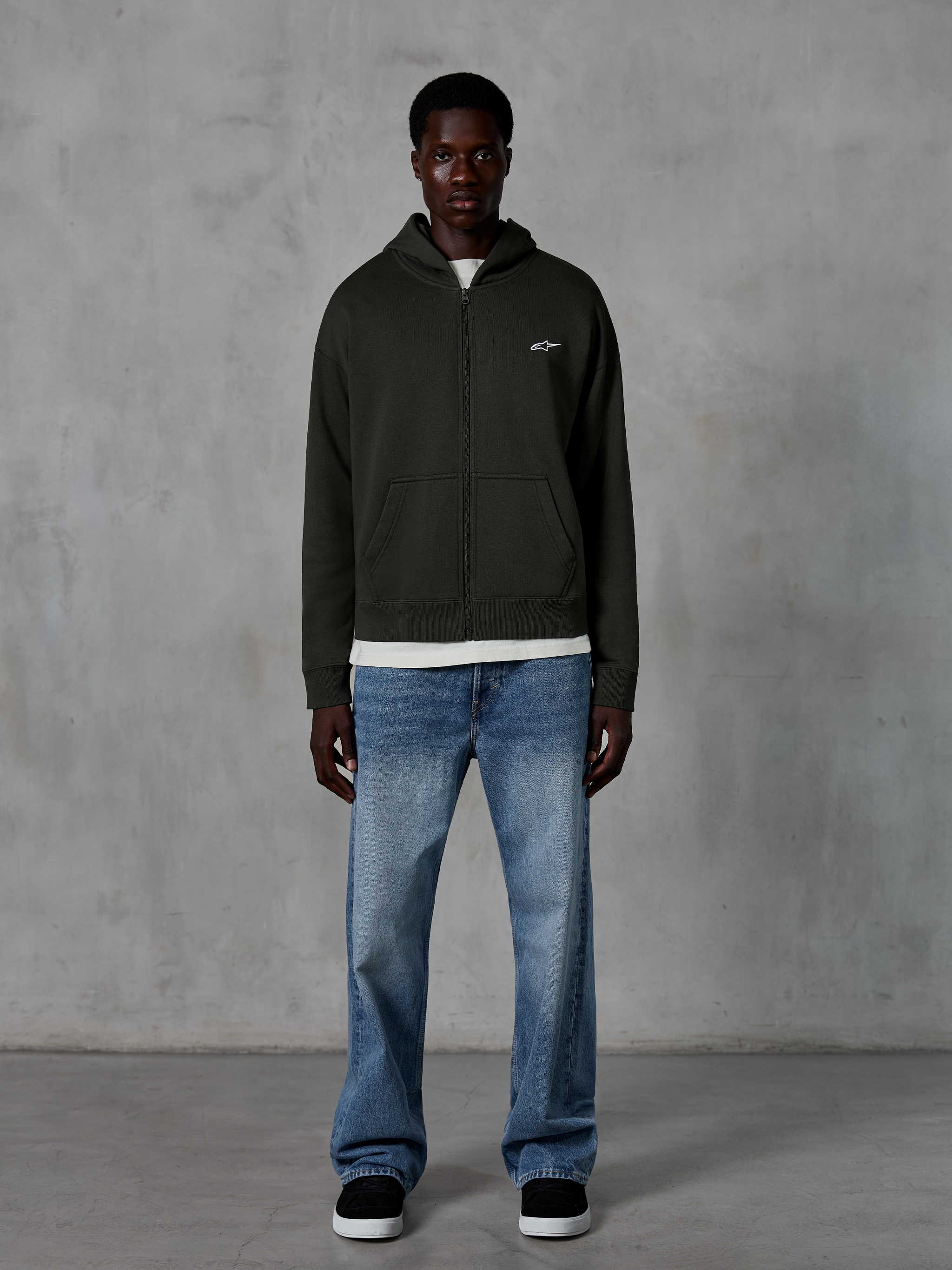 Alpinestars Essentials Ageless Zip Hoodie, Full-Zip Hoodie, Off Black, featuring a small white Alpinestars logo on the chest, worn by a model with a white t-shirt and blue jeans, relaxed fit, casual motorsport streetwear