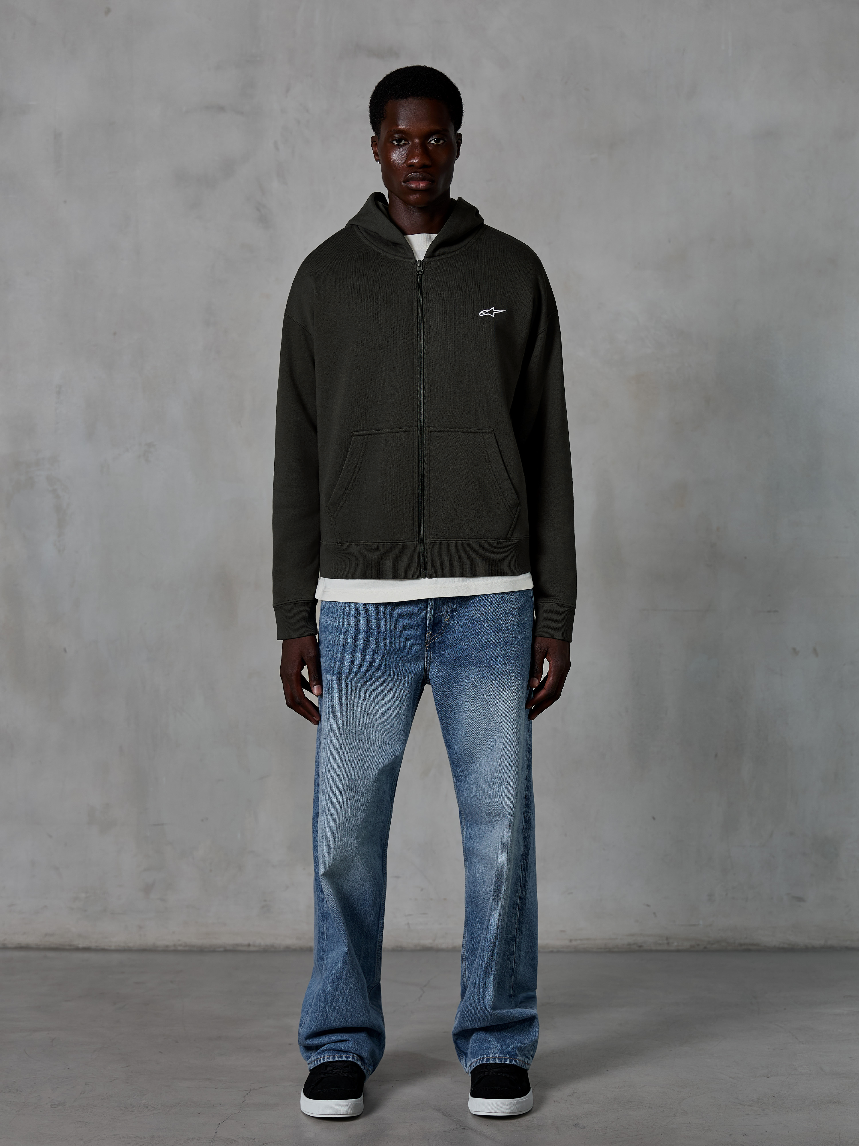 Alpinestars Essentials Ageless Zip Hoodie, Full-Zip Hoodie, Off Black, featuring a small white Alpinestars logo on the chest, worn by a model with a white t-shirt and blue jeans, relaxed fit, casual motorsport streetwear