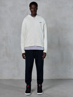 Alpinestars Essentials Ageless Zip Hoodie, Off White full-zip hoodie, relaxed fit with small black logo on chest, worn with black sweatpants and sneakers, casual motorsport-inspired streetwear.
