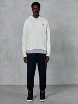 Alpinestars Essentials Ageless Zip Hoodie, off-white hoodie met volledige rits, ontspannen pasvorm met een klein zwart logo op de borst, gedragen met een zwarte joggingbroek en sneakers, casual motorsport-geïnspireerde streetwear.