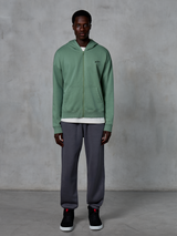 Alpinestars Essentials Ageless Zip Hoodie, hoodie met rits, Cactus Green, gedragen door een model met donkergrijze joggers en zwarte sneakers, klein zwart Alpinestars-logo op de borst, ontspannen pasvorm, casual streetwear