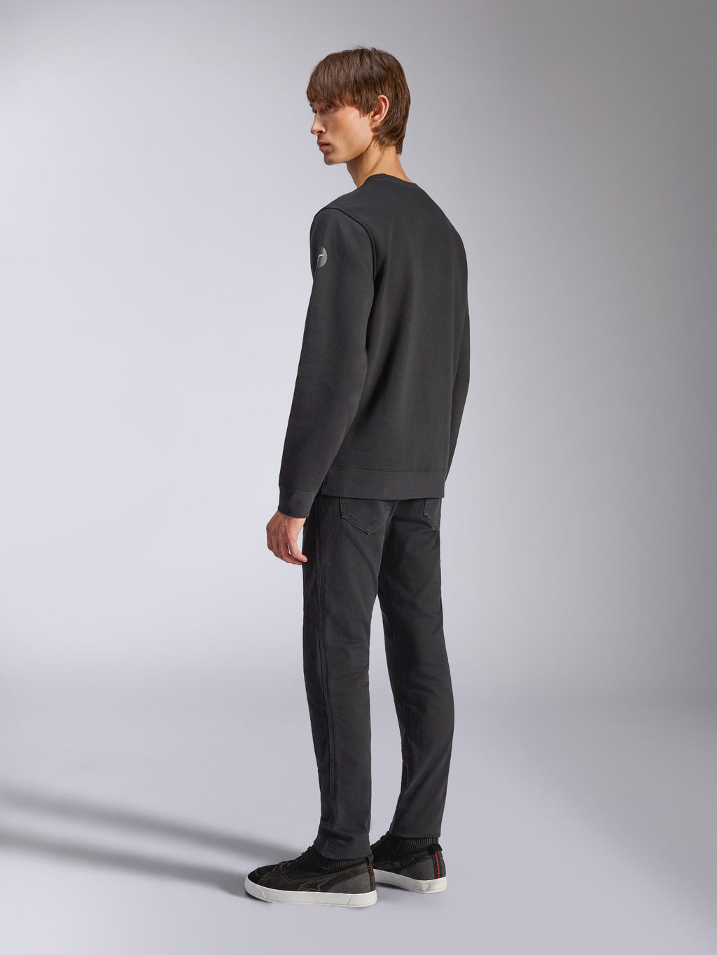 Alpinestars Bettern Crew, fleece pullover, zwart, mannelijk model getoond vanuit een achter- en zijaanzicht, voorzien van geribbelde manchetten en zoom met een klein logo op de mouw, casual motorsport-geïnspireerde streetwear