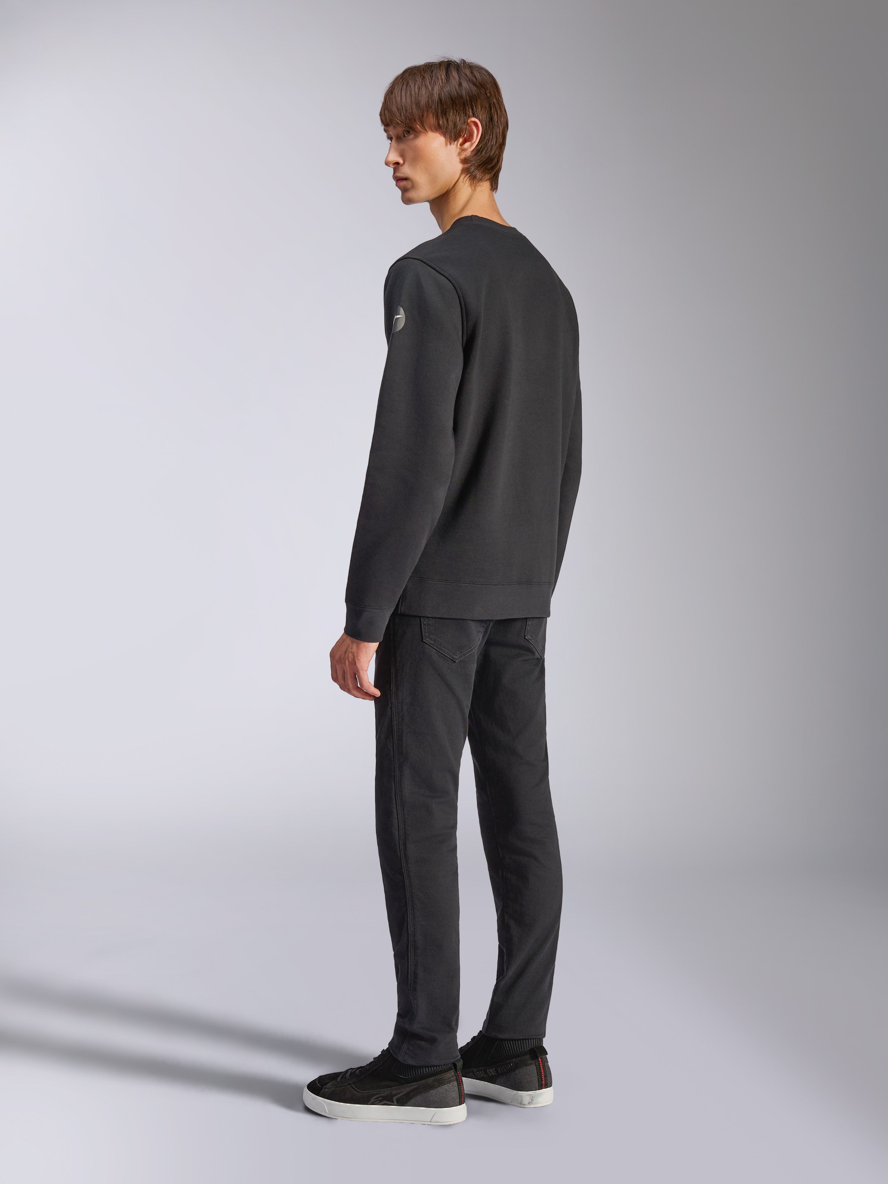 Alpinestars Bettern Crew, fleece pullover, zwart, mannelijk model getoond vanuit een achter- en zijaanzicht, voorzien van geribbelde manchetten en zoom met een klein logo op de mouw, casual motorsport-geïnspireerde streetwear
