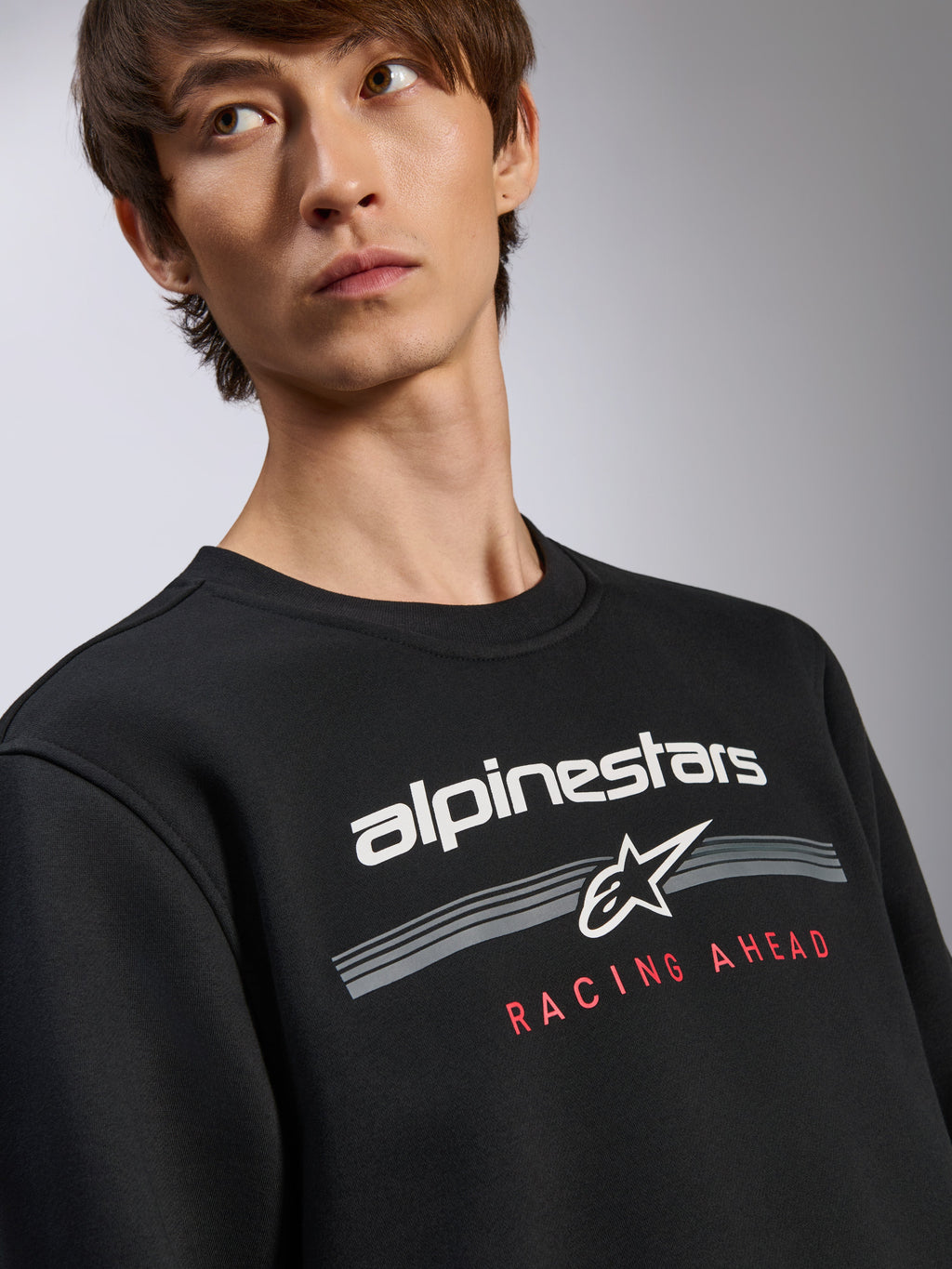 Alpinestars Bettern Crew Pullover, zwart sweatshirt, wit Alpinestars-logo met rode 'Racing Ahead' tekstgrafiek, ronde hals, casual motorsport-geïnspireerde streetwear