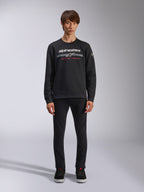 Alpinestars Bettern Crew, zwarte sweatshirt met ronde hals, wit Alpinestars-logo met grijze horizontale strepen en rode 'RACING AHEAD' tekst, casual motorsport streetwear, gedragen door model met zwarte broek en sneakers