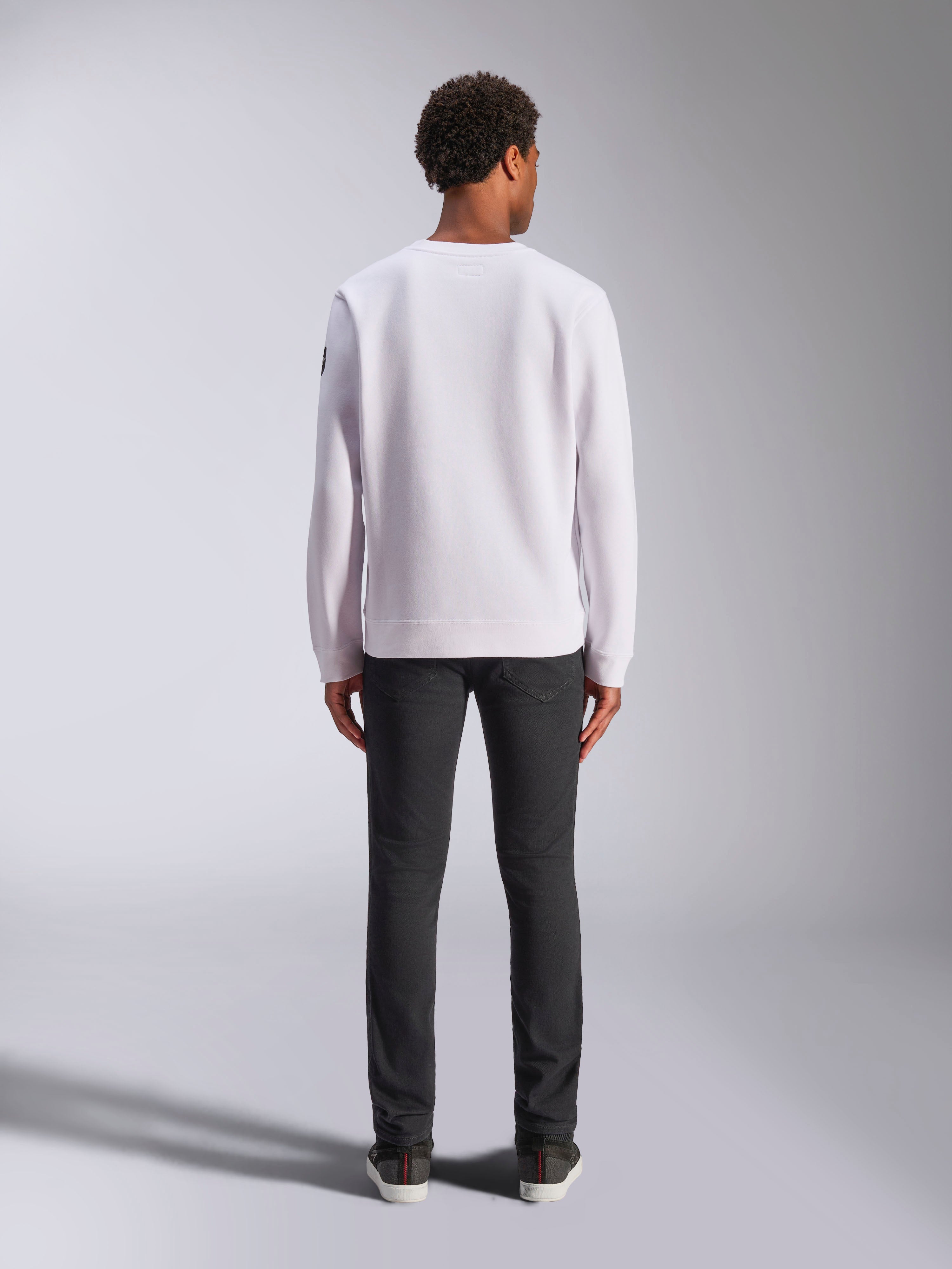 Alpinestars Bettern Crew, wit sweatshirt met ronde hals, achteraanzicht op model, gecombineerd met donkere jeans en sneakers, casual motorsport-geïnspireerde streetwear