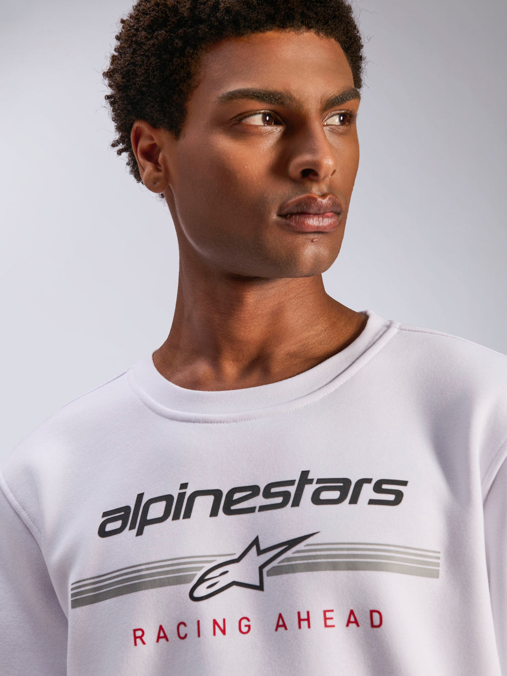 Alpinestars Bettern Crew, witte fleece crewneck, zwart Alpinestars logo met grijze horizontale strepen en rode 'Racing Ahead' tekst, casual motorsport-geïnspireerde streetwear