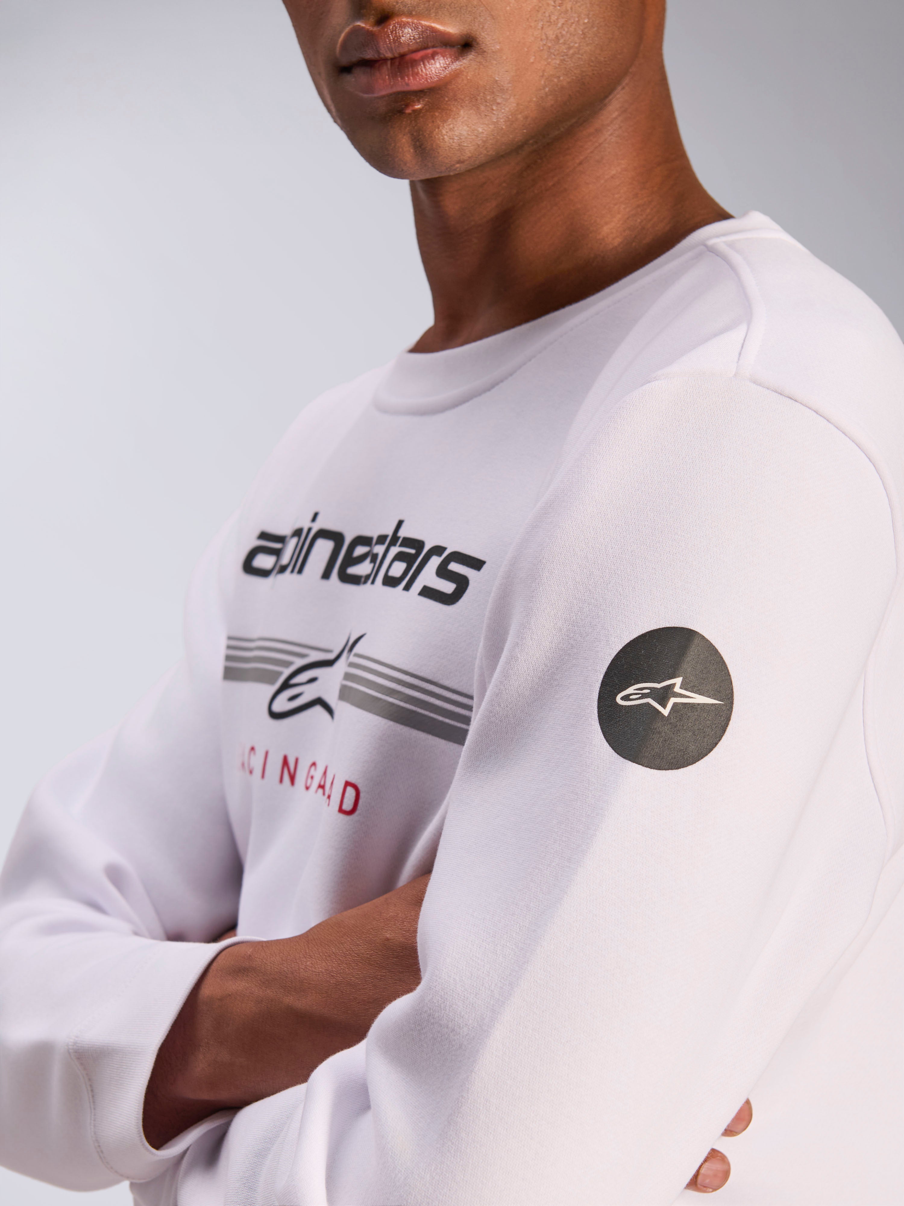 Alpinestars Bettern Crew, witte sweatshirt met ronde hals, casual motorsport streetwear, met grafische print op de borst met Alpinestars-woordmerk en grijze strepen, zwarte ronde patch met sterlogo op de mouw, fleece pullover ontwerp