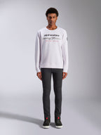 Alpinestars Bettern Crew, witte sweatshirt met ronde hals, gedragen door mannelijk model met donkergrijze broek en zwarte hoge sneakers, voorzien van Alpinestars-branding met rode 'Racing Ahead' tekst, casual op motorsport geïnspireerde streetwear