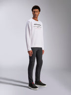 Alpinestars Bettern Crew, witte pullover sweatshirt, met zwart Alpinestars-logo en rode 'Racing Ahead'-tekst, casual motorsport streetwear, gedragen door een model met donkere broek en zwarte sneakers