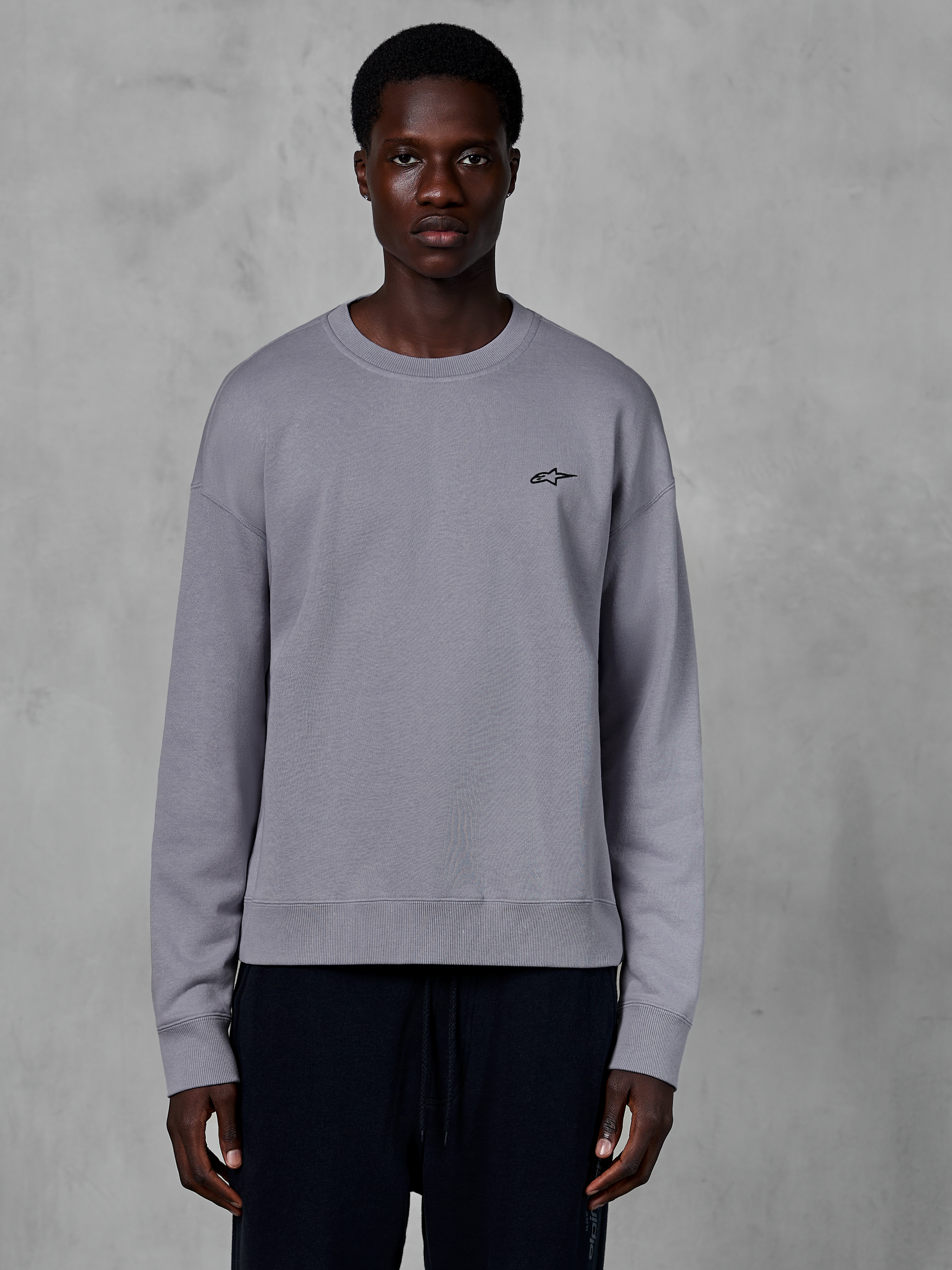 Alpinestars Essentials Ageless Crew, zilverkleurige sweatshirt met ronde hals gedragen door een model, voorzien van een klein zwart sterlogo op de borst, ontspannen pasvorm met geribbelde manchetten en zoom, casual motorsport streetwear