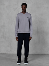 Alpinestars Essentials Ageless Crew, zilverkleurig sweatshirt met ronde hals, gedragen door een model met zwarte joggingbroek en zwarte sneakers, voorzien van een klein zwart Alpinestars-logo op de borst, casual op motorsport geïnspireerde streetwear