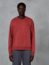 Alpinestars Essentials Ageless Crew, crewneck sweatshirt, steenrood, klein zwart logo op de borst, gedragen door een model met een grijze broek, premium zachte fleece casual streetwear