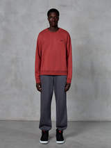 Alpinestars Essentials Ageless Crew, Brick Red crewneck sweatshirt, gedragen met een grijze joggingbroek en zwarte sneakers, voorzien van een klein zwart logo op de borst, casual motorsport-geïnspireerde streetwear