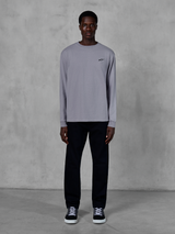 Alpinestars Essentials Ageless LS Tee, T-shirt met lange mouwen, zilver, klein zwart Alpinestars-logo op de borst, biologisch katoenen jersey met stone wash afwerking, gedragen door een model met zwarte broek en sneakers, casual streetwear