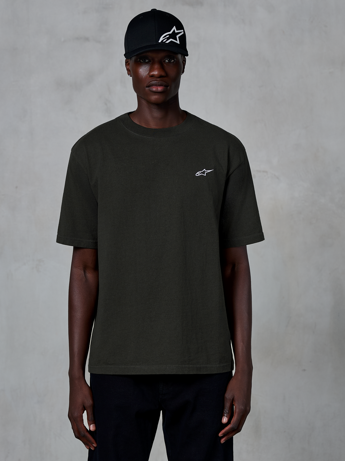 Alpinestars Essentials Ageless SS Tee, T-shirt met korte mouwen, Off Black, gedragen door een model met een zwarte pet met logo, klein wit Alpinestars-logo op de borst, casual motorsport-geïnspireerde streetwear