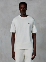 Alpinestars Essentials Ageless SS Tee, T-shirt met korte mouwen, Off White, gedragen door een mannelijk model, voorzien van een klein zwart Alpinestars-logo op de borst, relaxte pasvorm, biologisch katoenen jersey, casual motorsport streetwear