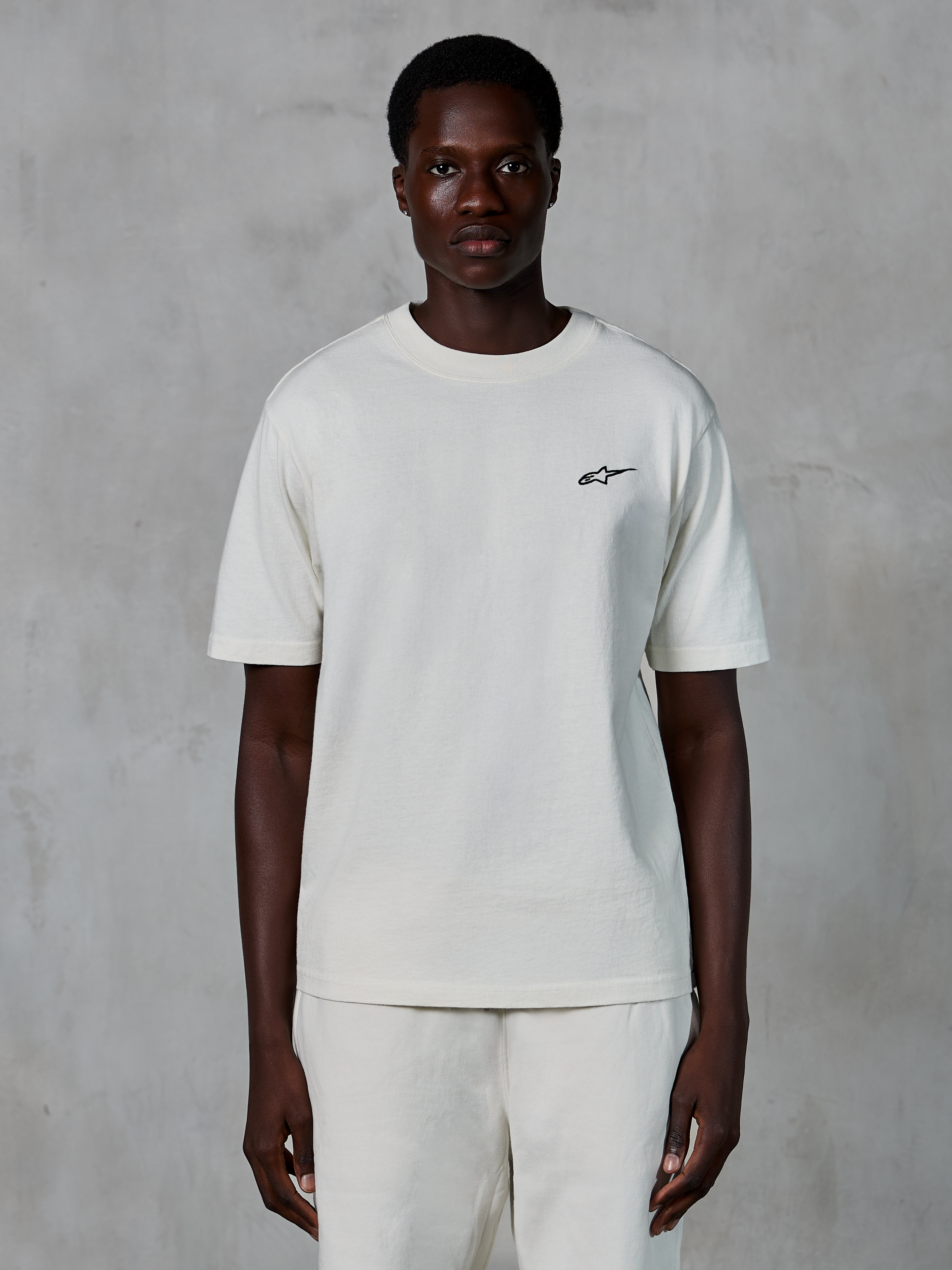 Alpinestars Essentials Ageless SS Tee, Short Sleeve T-Shirt, Off White, worn by a male model, featuring a small black Alpinestars logo on the chest, relaxed fit, organic cotton jersey, casual motorsport streetwear