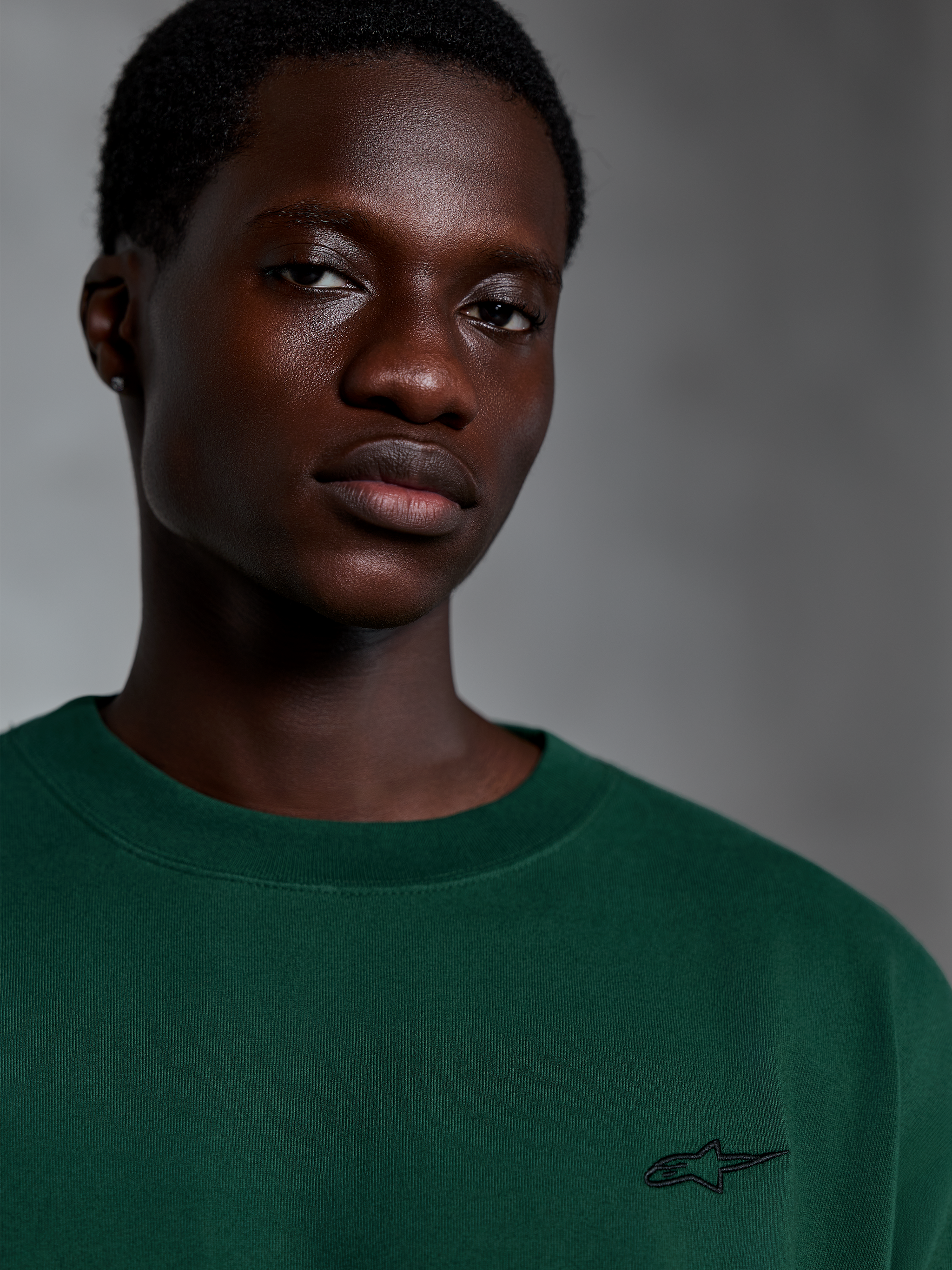 Alpinestars Essentials Ageless SS Tee, Pine Green T-shirt met korte mouwen, close-up van model in een groen biologisch katoenen shirt met een klein geborduurd logo, casual streetwear-ontwerp