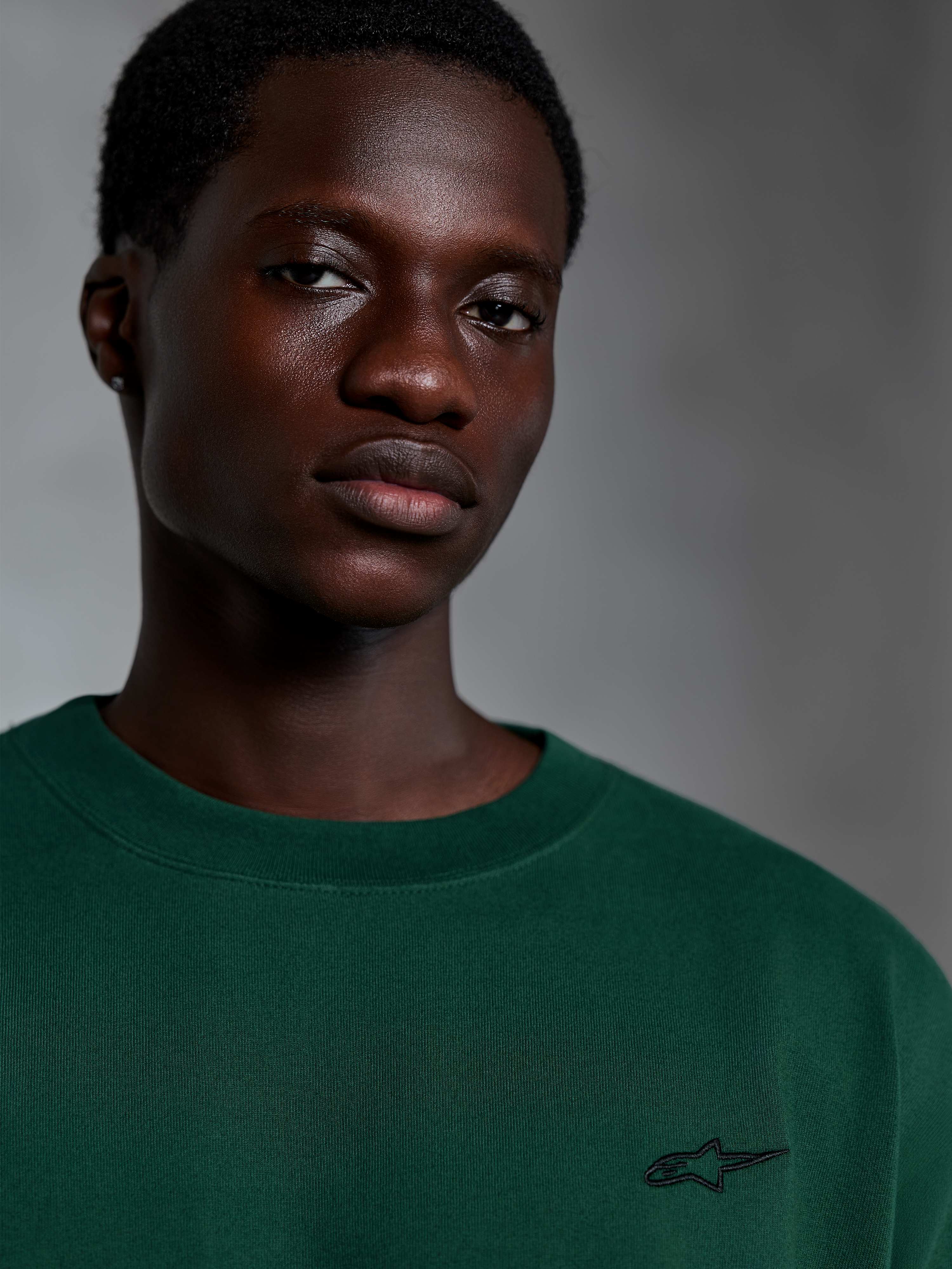 Alpinestars Essentials Ageless SS Tee, Pine Green T-shirt met korte mouwen, close-up van model in een groen biologisch katoenen shirt met een klein geborduurd logo, casual streetwear-ontwerp