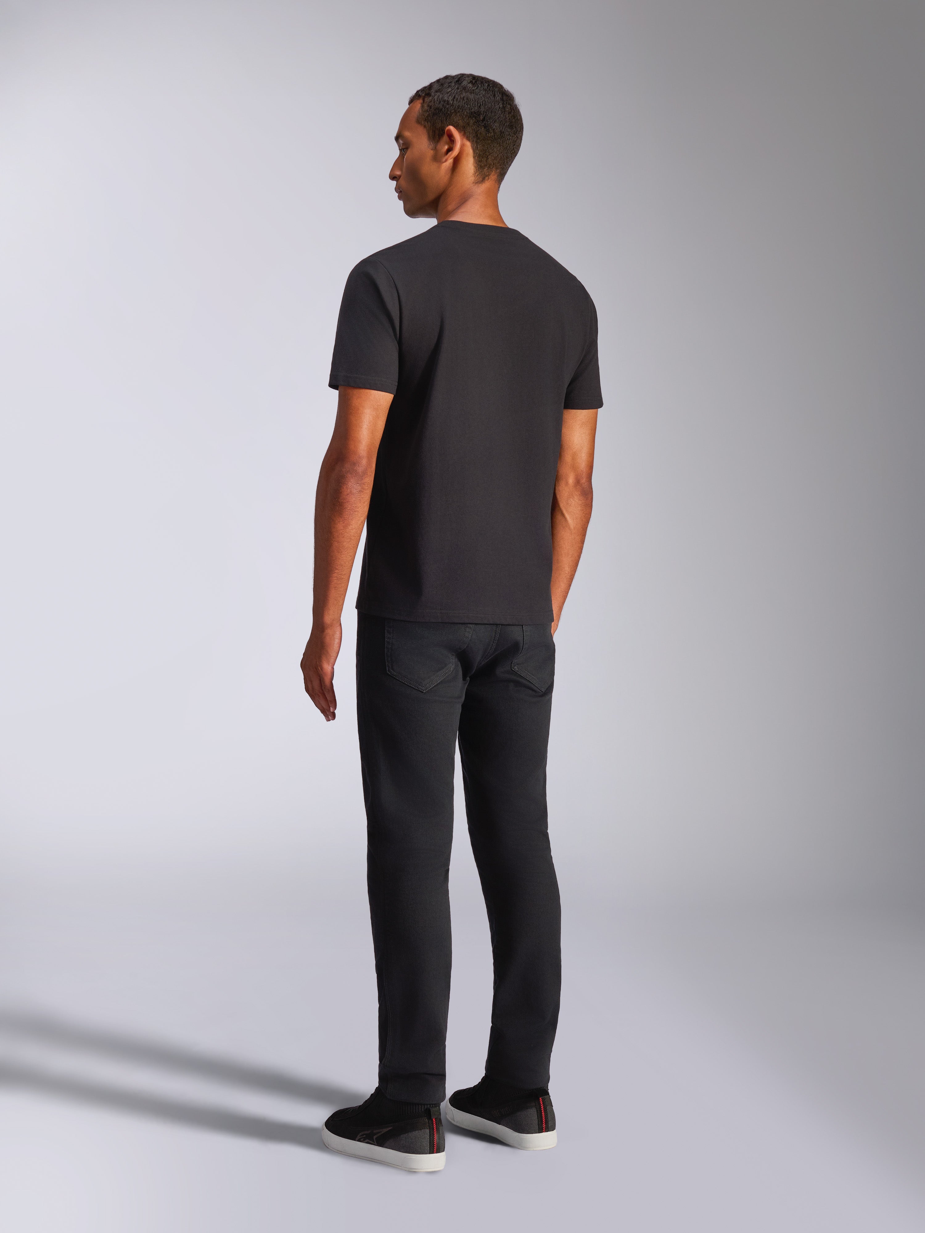 Alpinestars Shaded CSF Tee, zwart T-shirt met korte mouwen, achteraanzicht van mannelijk model dat een zwarte broek en vrijetijdsschoenen draagt, lifestyle motorsportkleding