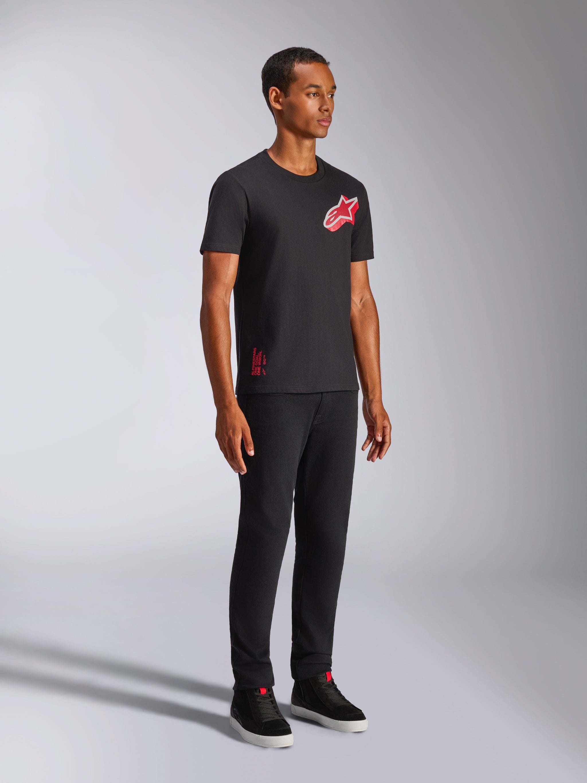 Alpinestars Shaded CSF Tee, T-shirt met korte mouwen, zwart, rood en wit schuin verlopend folieprint Astars-logo, casual motorsport streetwear, volledige opname van een model met zwarte broek en sneakers