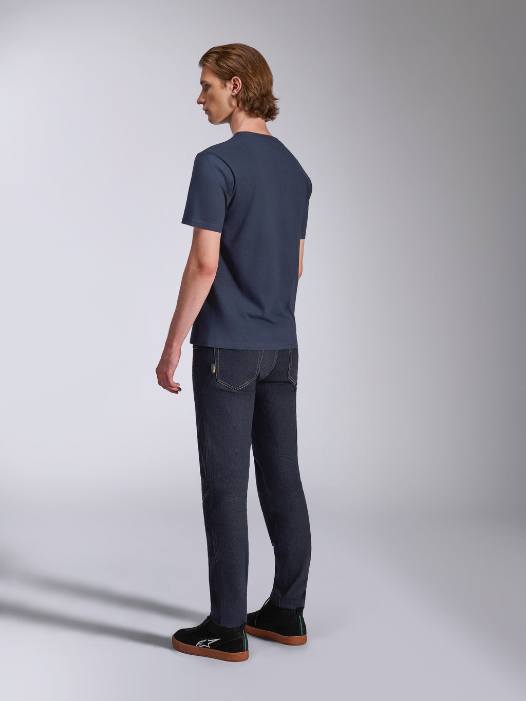 Alpinestars Fasting CSF Tee, T-shirt met korte mouwen, marineblauw, achteraanzicht op model, gecombineerd met een donkere denim broek en zwarte sneakers, casual motorsport-geïnspireerde streetwear