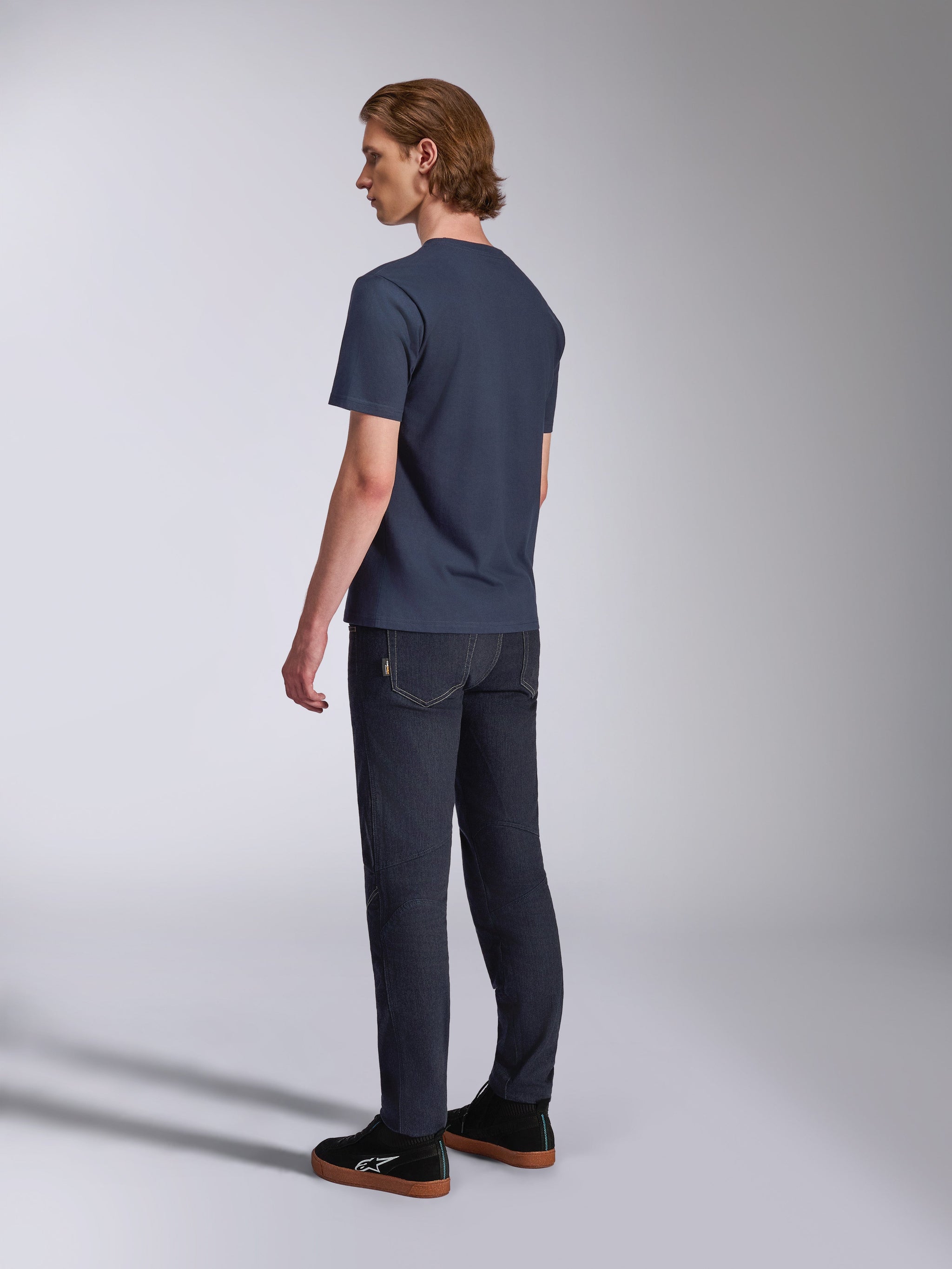 Alpinestars Fasting CSF Tee, T-shirt met korte mouwen, marineblauw, achteraanzicht op model, gecombineerd met een donkere denim broek en zwarte sneakers, casual motorsport-geïnspireerde streetwear