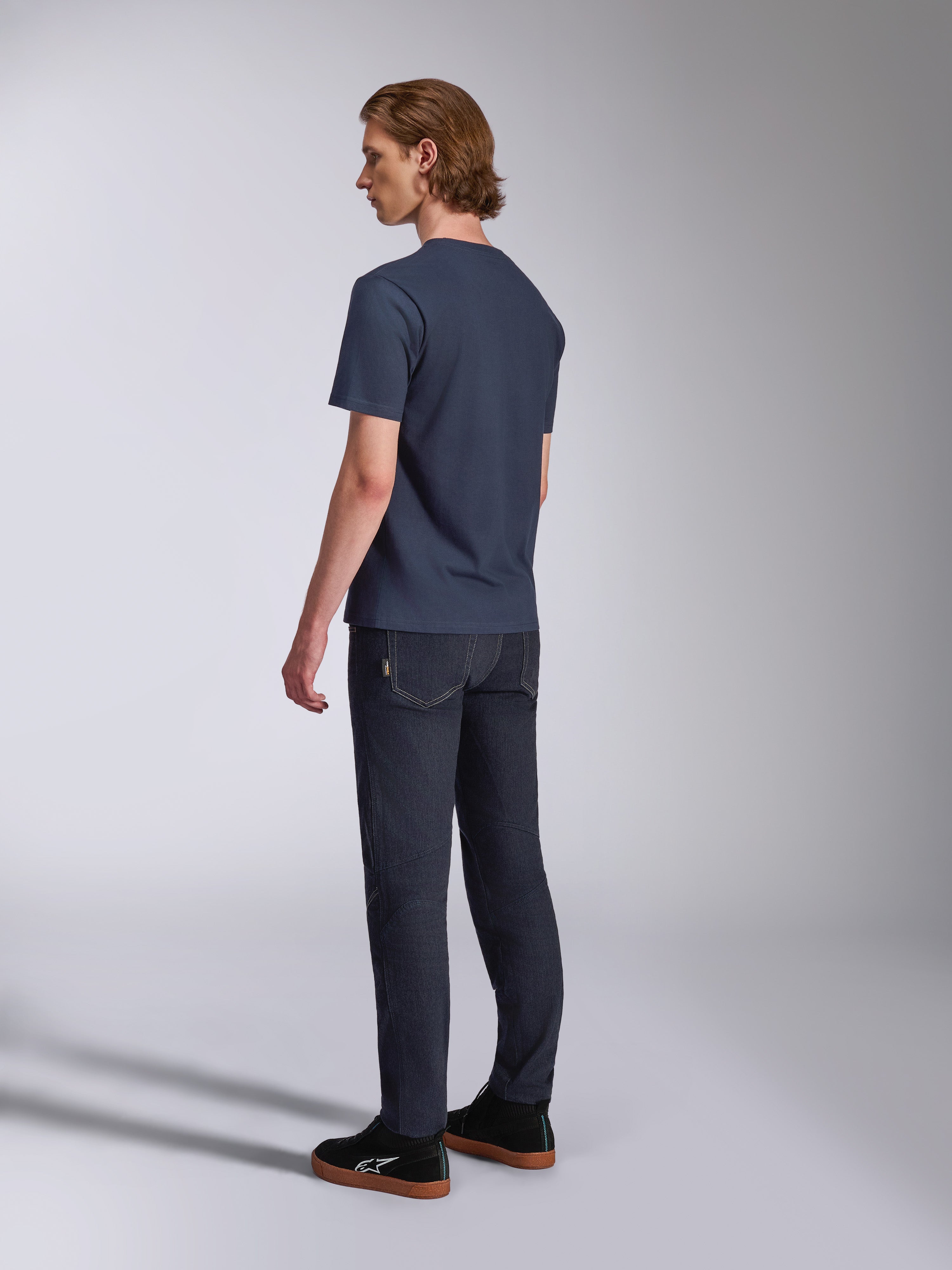 Alpinestars Fasting CSF Tee, T-shirt met korte mouwen, marineblauw, achteraanzicht op model, gecombineerd met een donkere denim broek en zwarte sneakers, casual motorsport-geïnspireerde streetwear